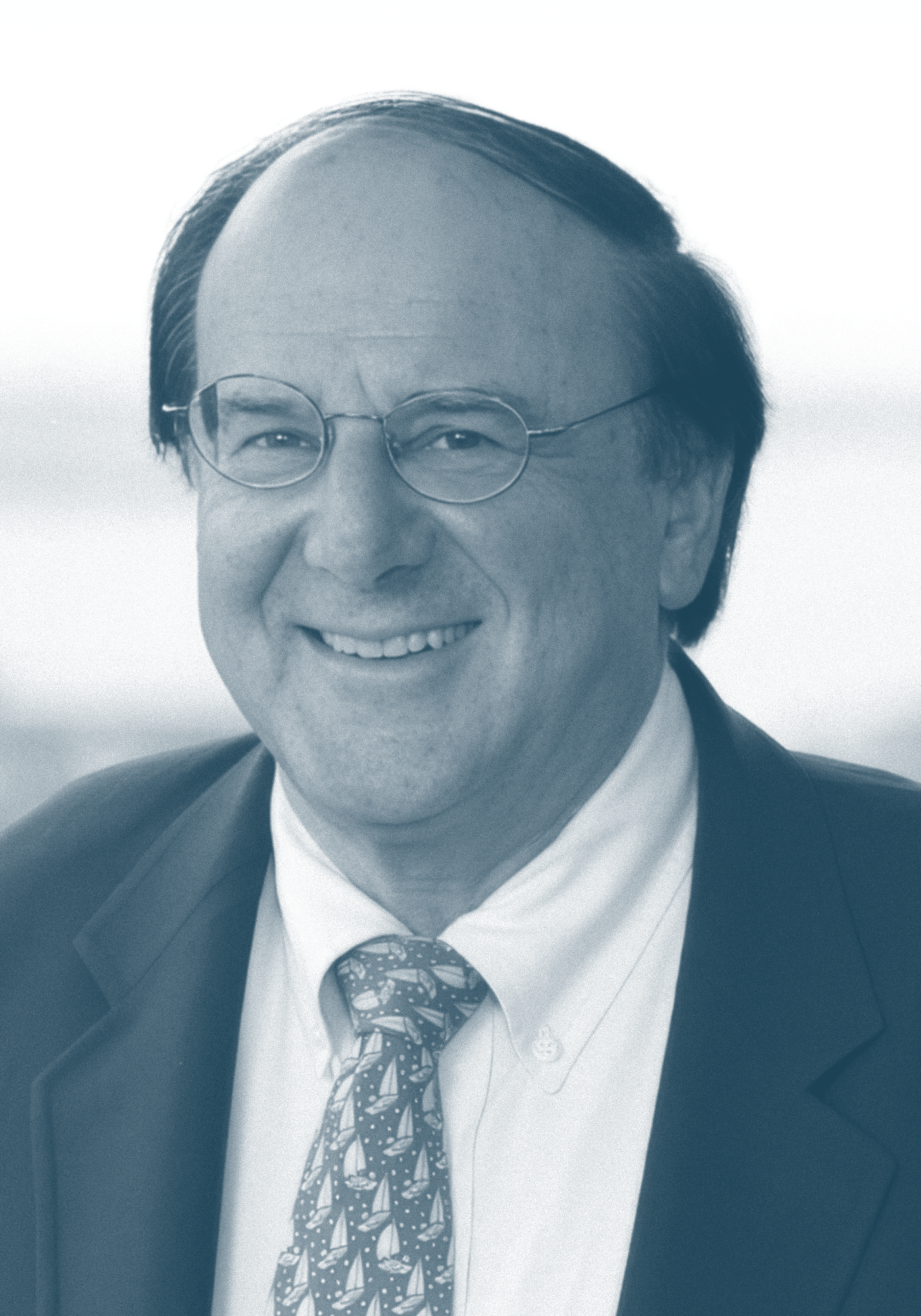 A smiling man wearing glasses, a suit, a white shirt, and a patterned tie.