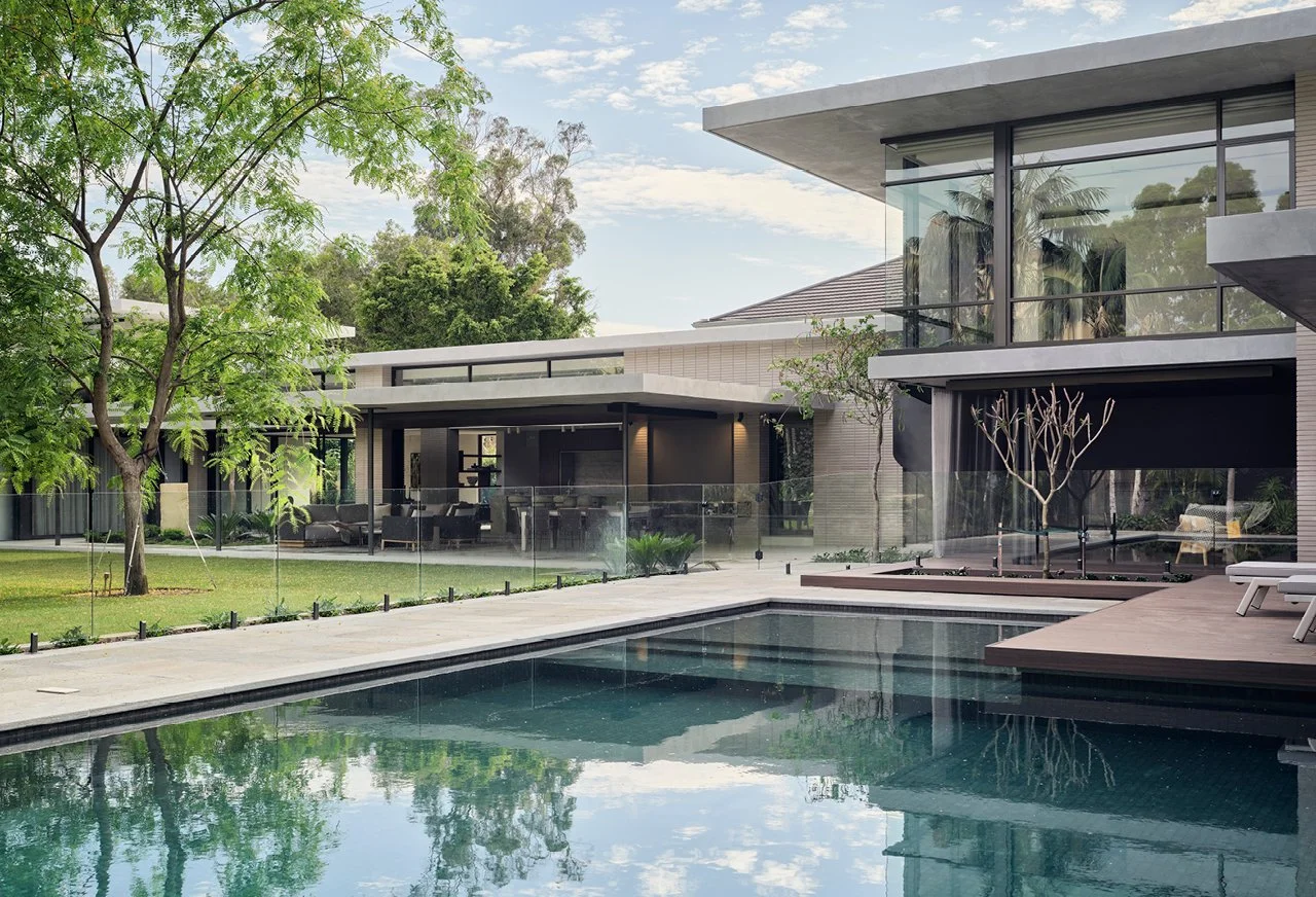 Modern house with a swimming pool in the backyard, surrounded by trees and greenery, with glass walls and patio furniture.