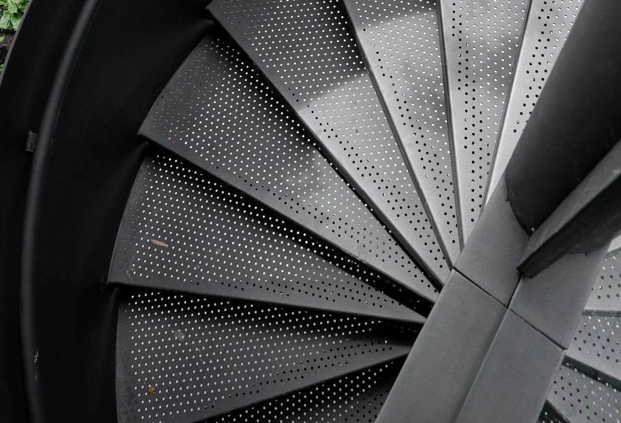 A close-up view of a modern spiral staircase with perforated metal treads and metal railing.