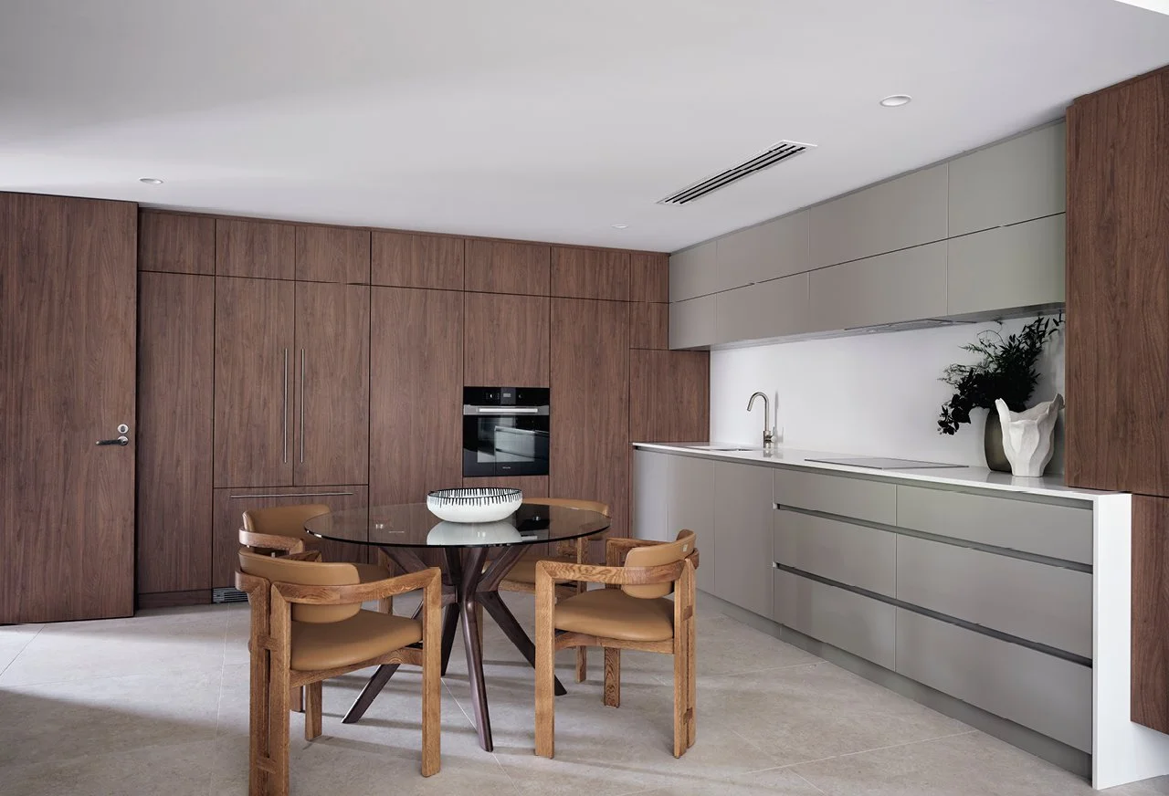 Modern kitchen with wooden cabinets, a round dining table with four chairs, a built-in oven, and decorative vases with plants.