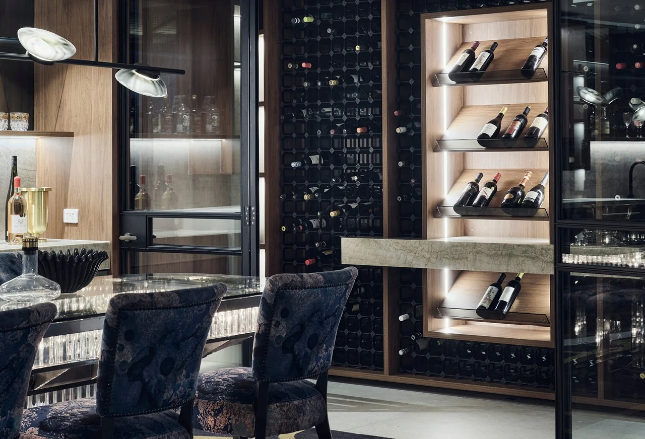 A modern wine cellar and dining area with a wine rack filled with bottles, a glass-top dining table, and upholstered chairs.