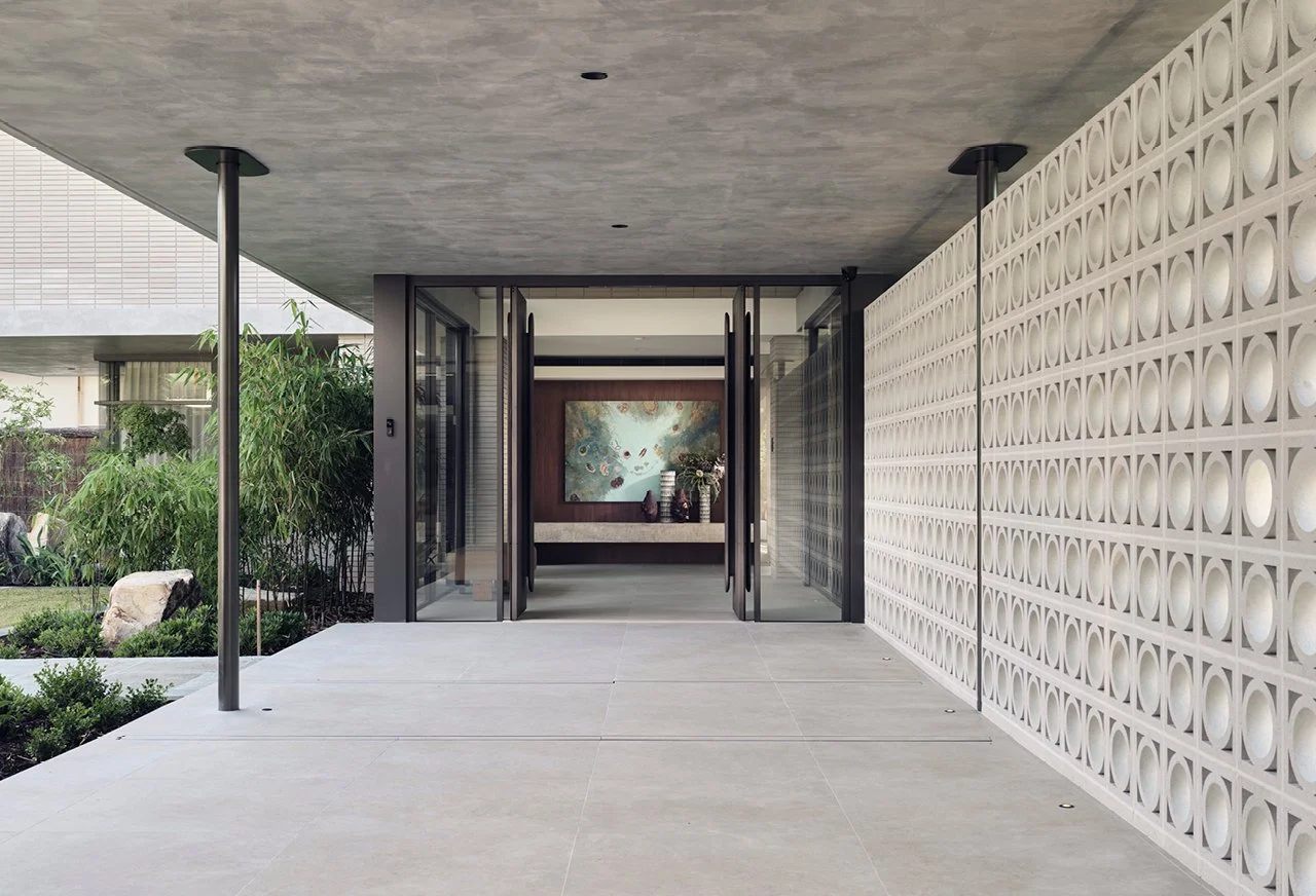 Modern building entrance with glass doors, decorative white wall, and outdoor greenery.
