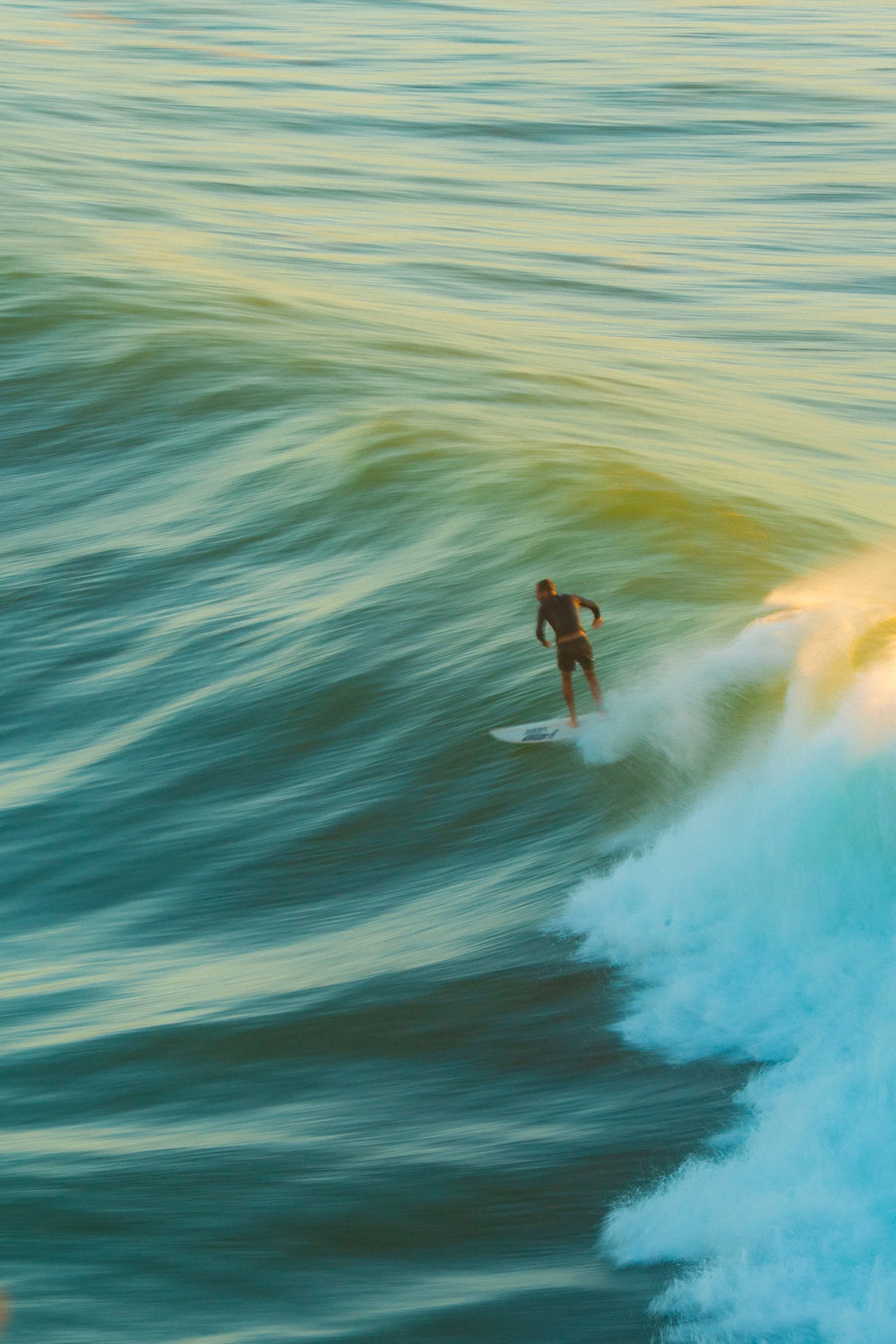 A person surfing on a large wave in the ocean, with the water appearing greenish and the sky overcast.