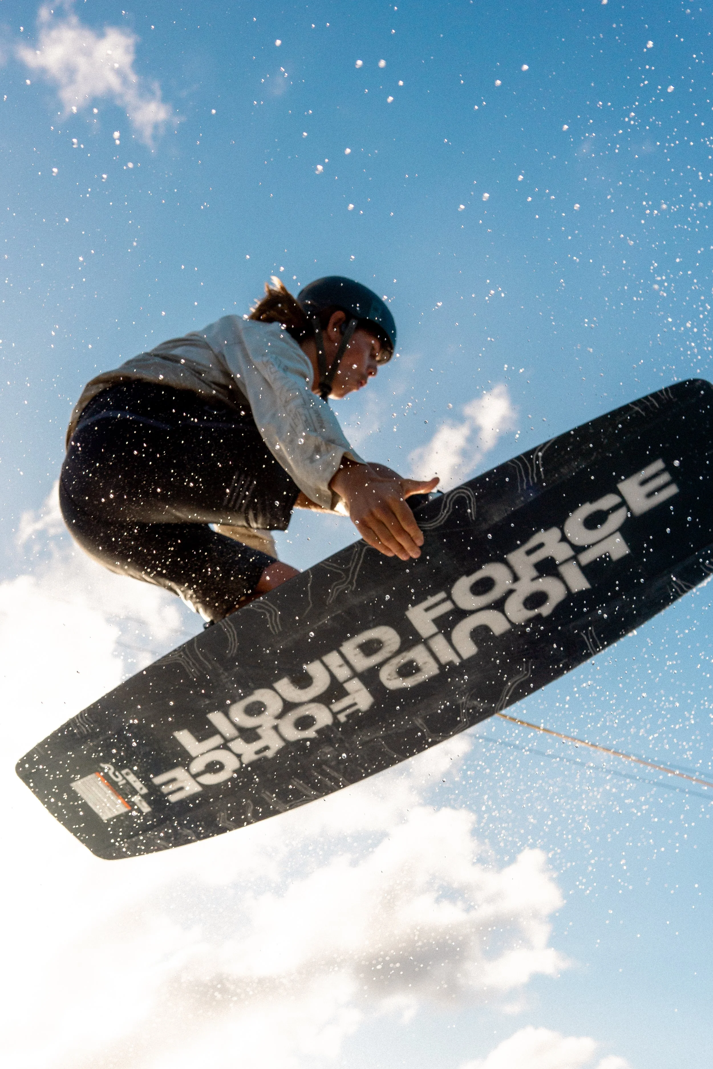 A person snowboarding in mid-air, wearing a helmet and outdoor gear, against a bright blue sky with clouds and snowflakes falling.