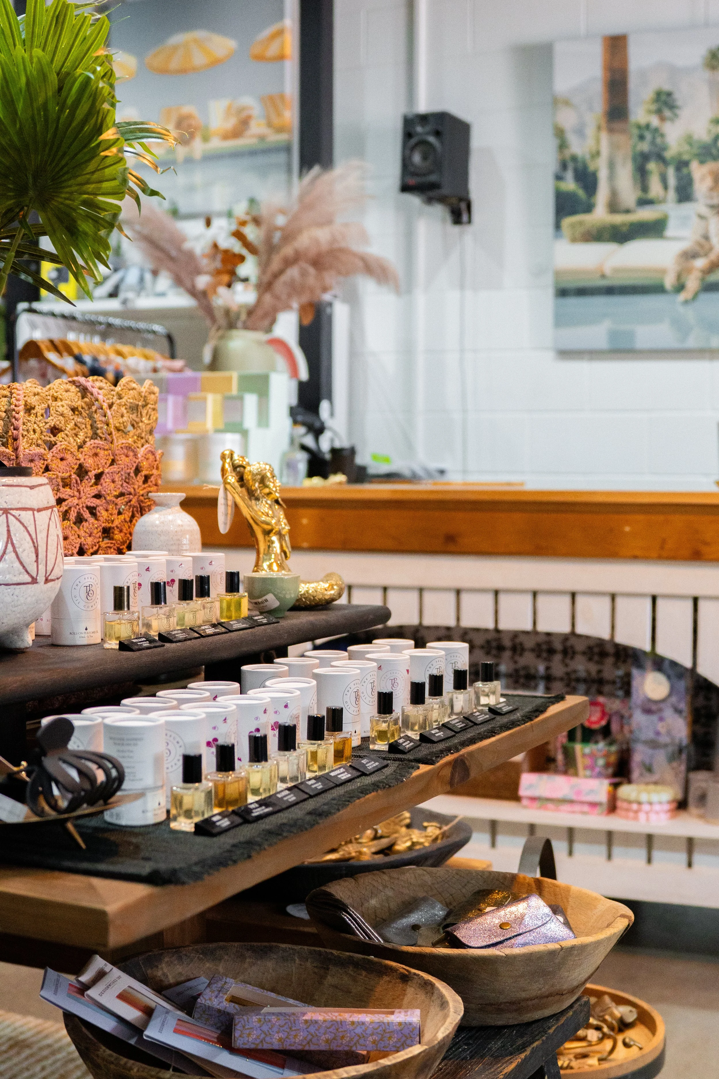 Display of various small bottles of perfume or essential oils, decorative items like a gold horse figurine and plant, on wooden tables in a boutique store.