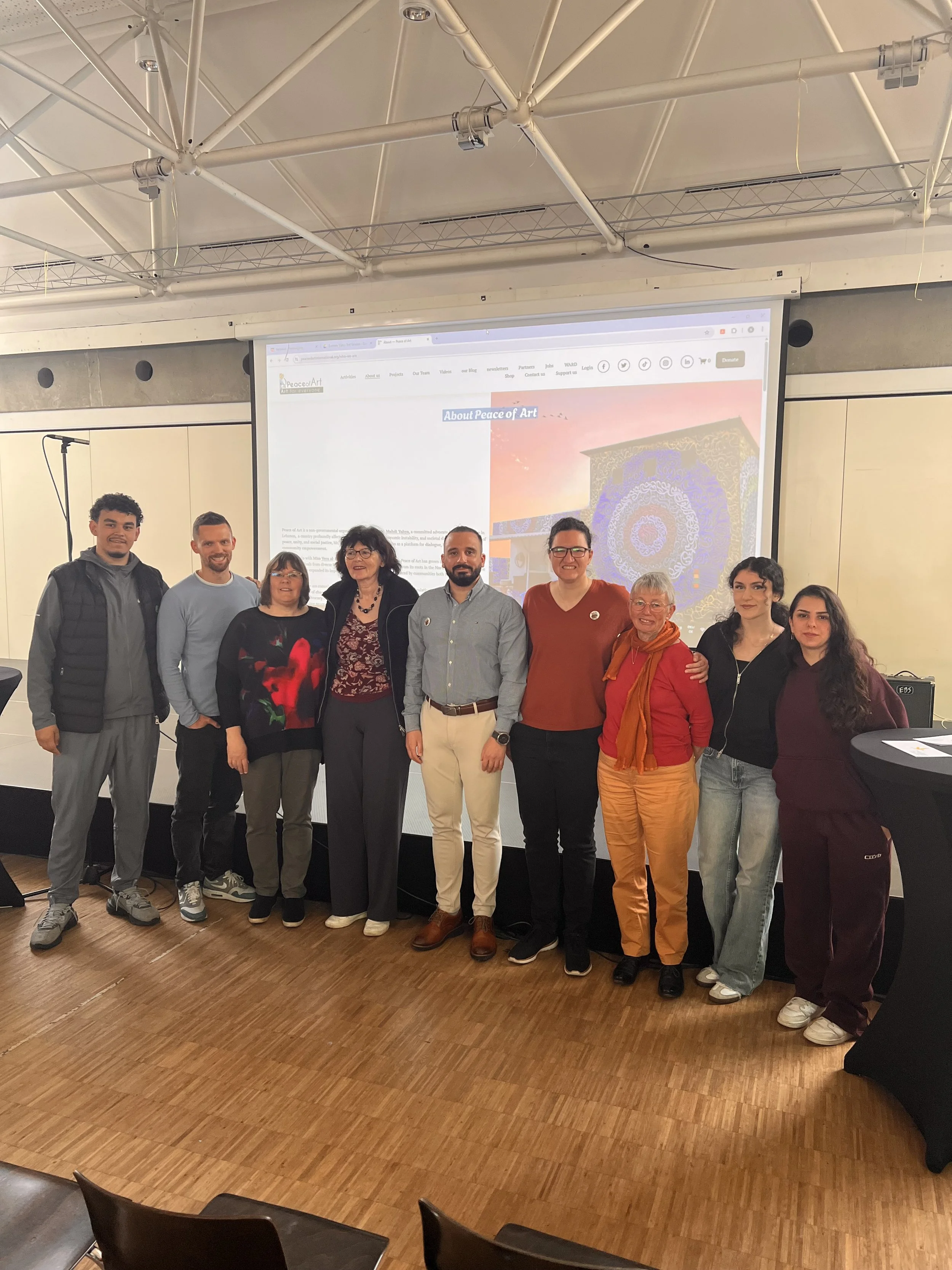 A group of eight people standing in a row in front of a projected presentation screen at a conference or event, smiling and posing for the photo.