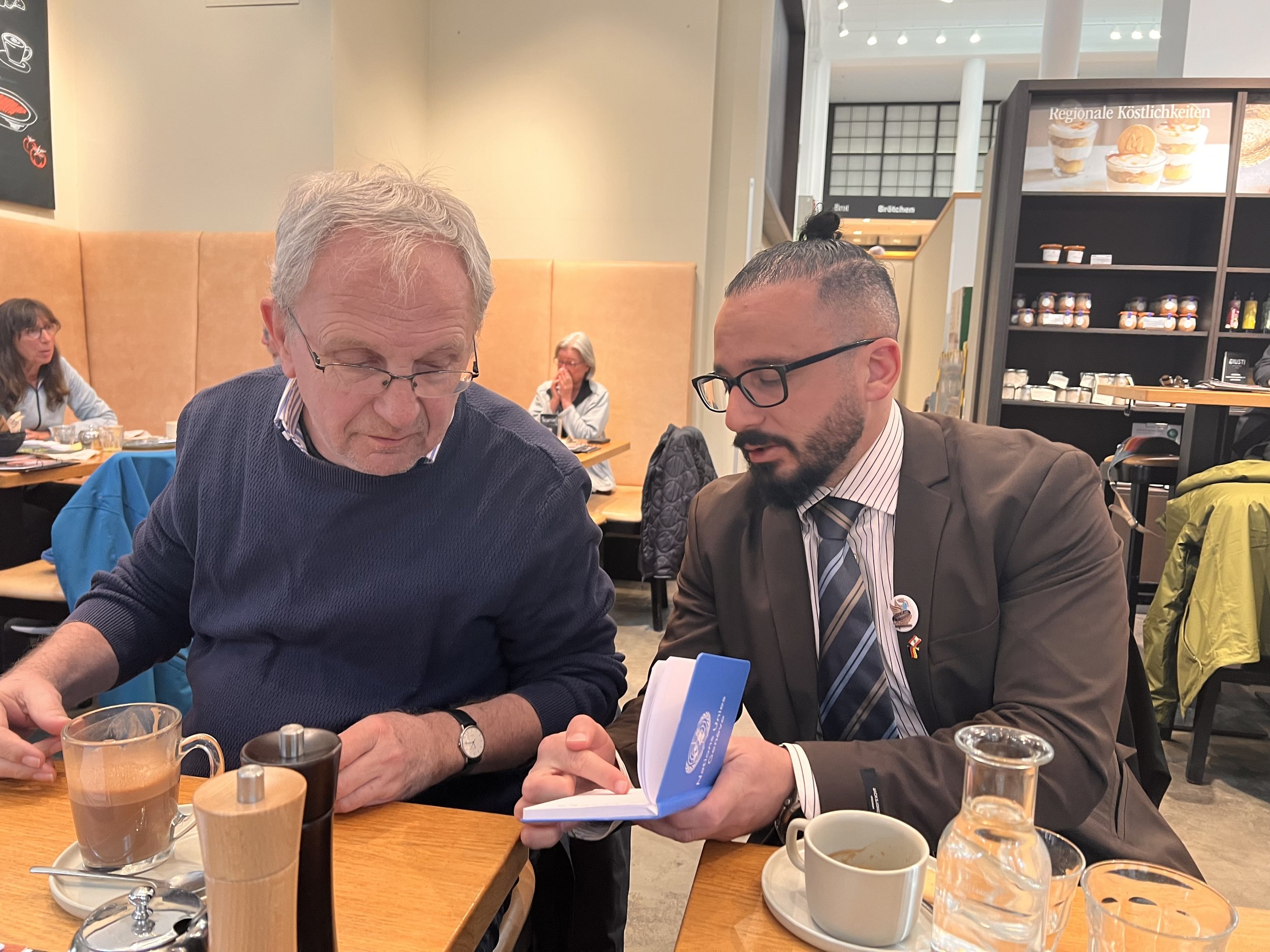 Mahdi Yahya and Anette’s husband seated together at a café, enjoying coffee and engaged in a deep and thoughtful conversation in a relaxed atmosphere.