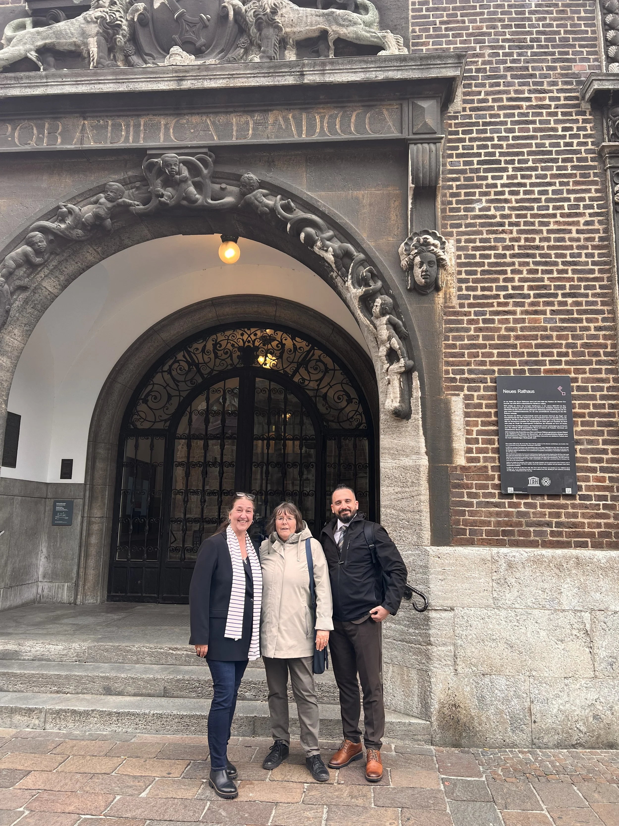 Mahdi Yahya, Anette, and a member of the Bremen Rathaus management team standing together in front of the historic Bremen City Hall. The group poses outside the landmark building, symbolizing collaboration, cultural exchange, and civic engagement.
