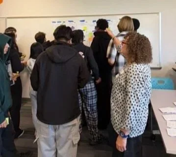 A group of students gathered around a whiteboard in a classroom.