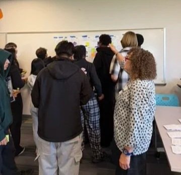 Students gathered around a whiteboard in a classroom, participating in a group activity or discussion.
