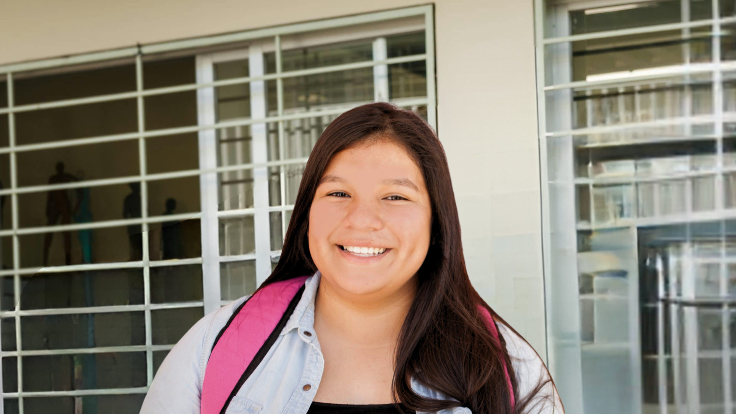 A smiling young woman with long dark hair wearing a white shirt and pink backpack, standing outside near glass windows.