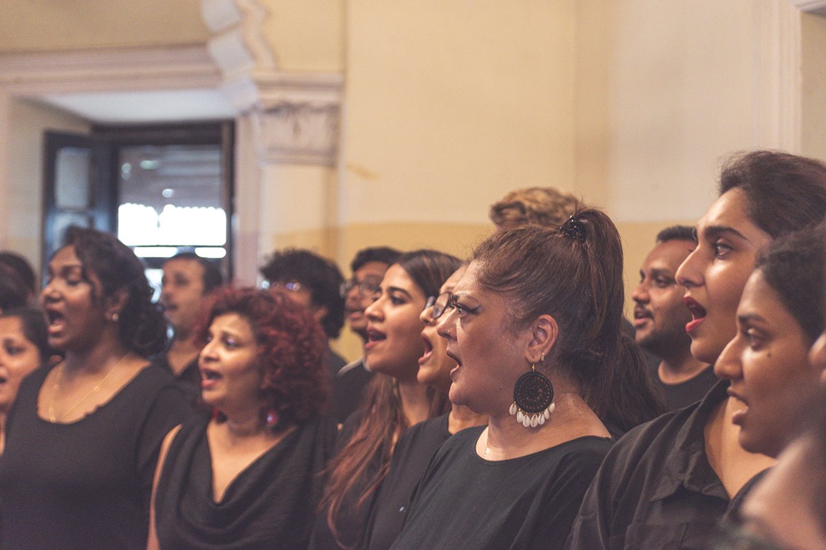A diverse group of people singing together during a choir or concert in an indoor venue.