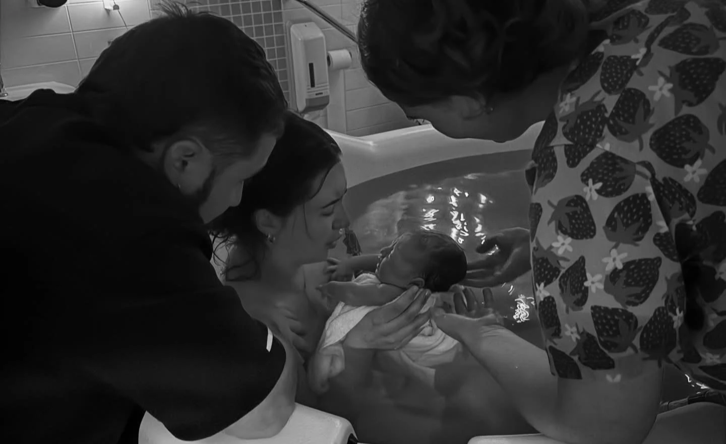 A newborn baby being held in a hospital setting with medical staff and a woman supporting the baby during a birth.