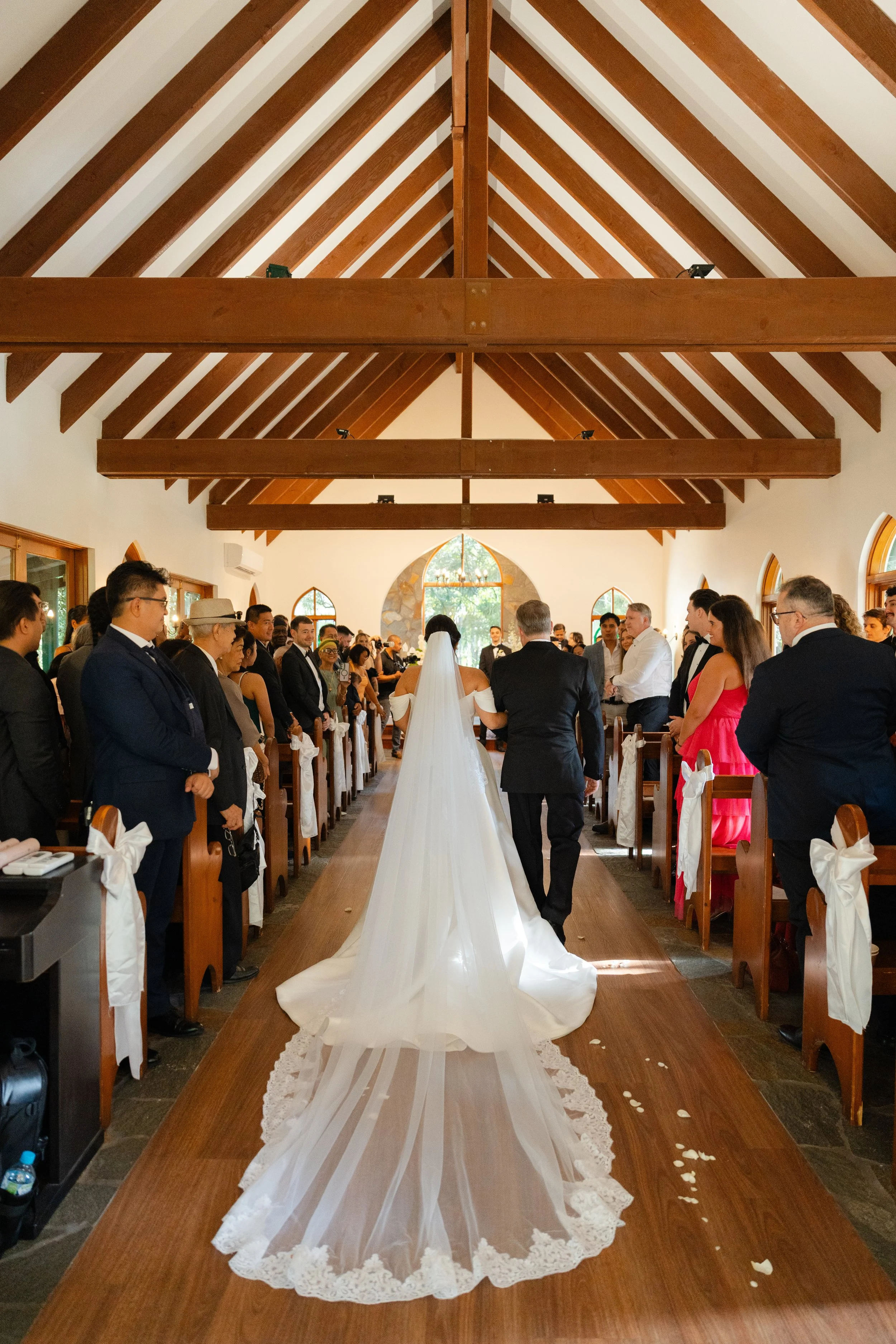 Bride and groom standing at the altar during a wedding ceremony inside a church with wooden beams on the ceiling. Guests are seated on either side, watching the couple.