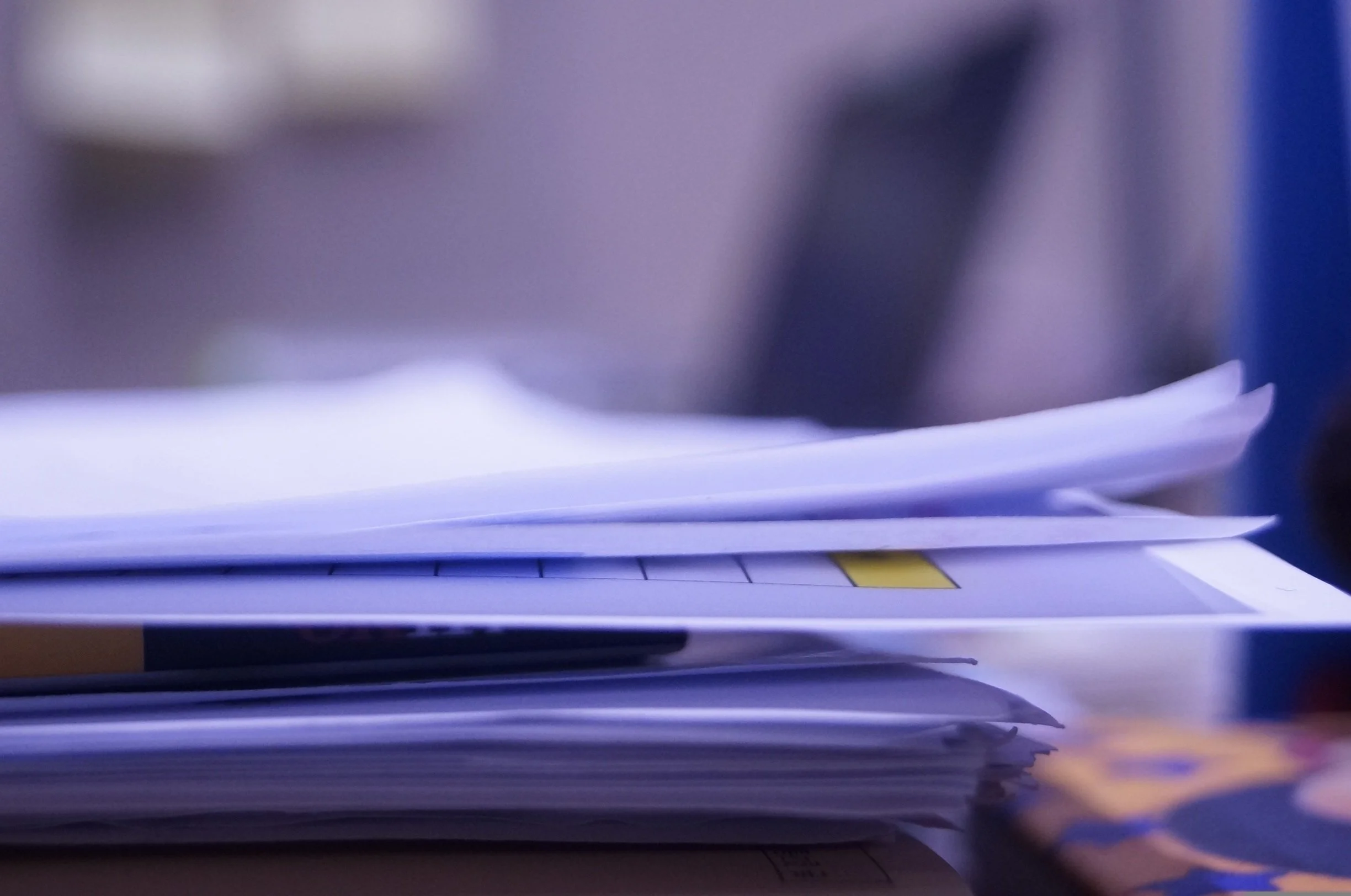 Blurred image of a stack of papers or documents on a desk with a dark background.
