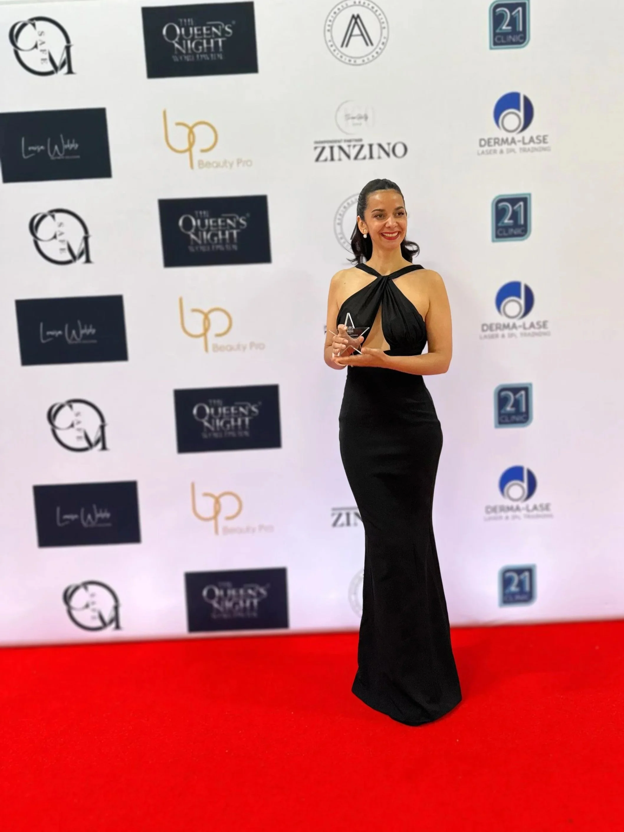 Award-winning PMU artist Bella Miguel holding her trophy at a beauty industry awards ceremony.