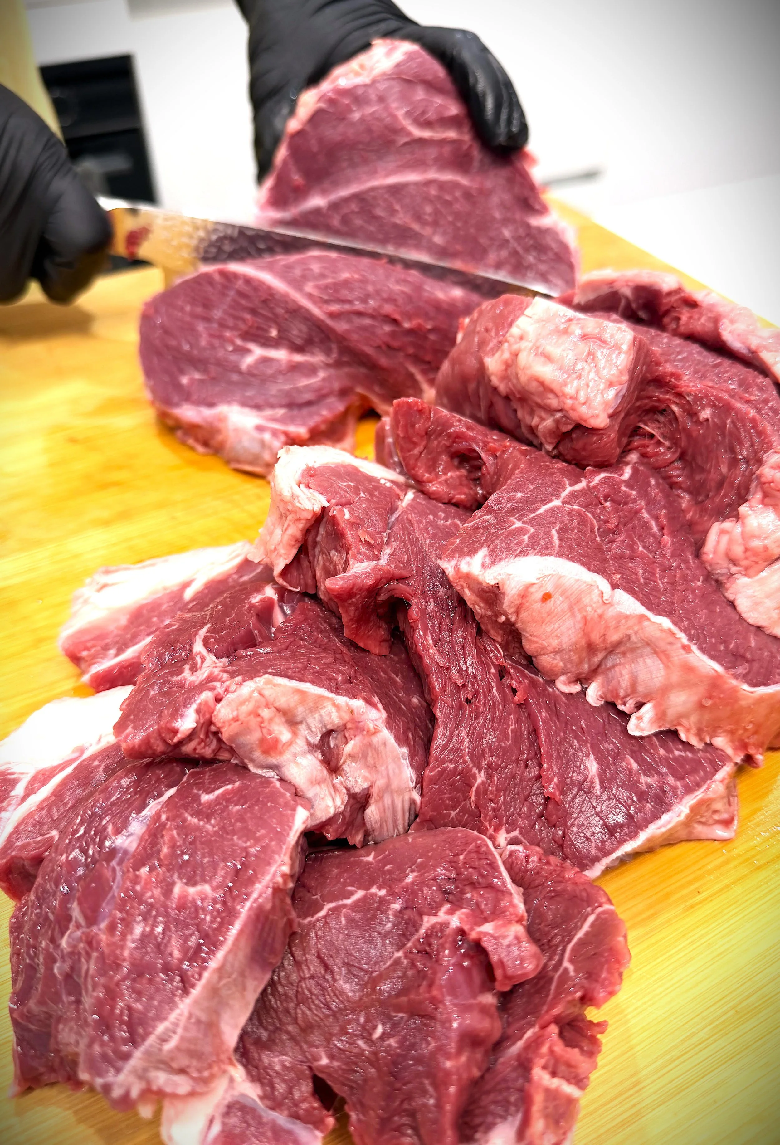 Sliced raw red meat on a yellow cutting board.