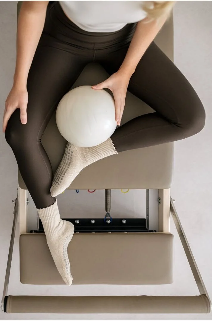 Personnes en position fœtale sur une table d'ostéopathie, tenant une balle blanche, portant un legging noir et des chaussettes blanches, vue du dessus.