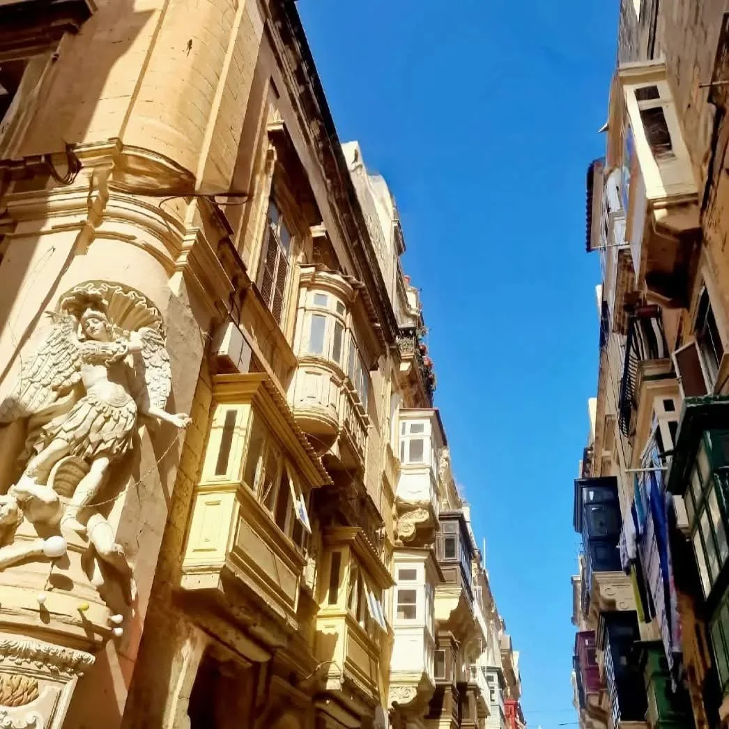 Street view of old European-style buildings with ornate architecture and decorative balconies, under a clear blue sky.