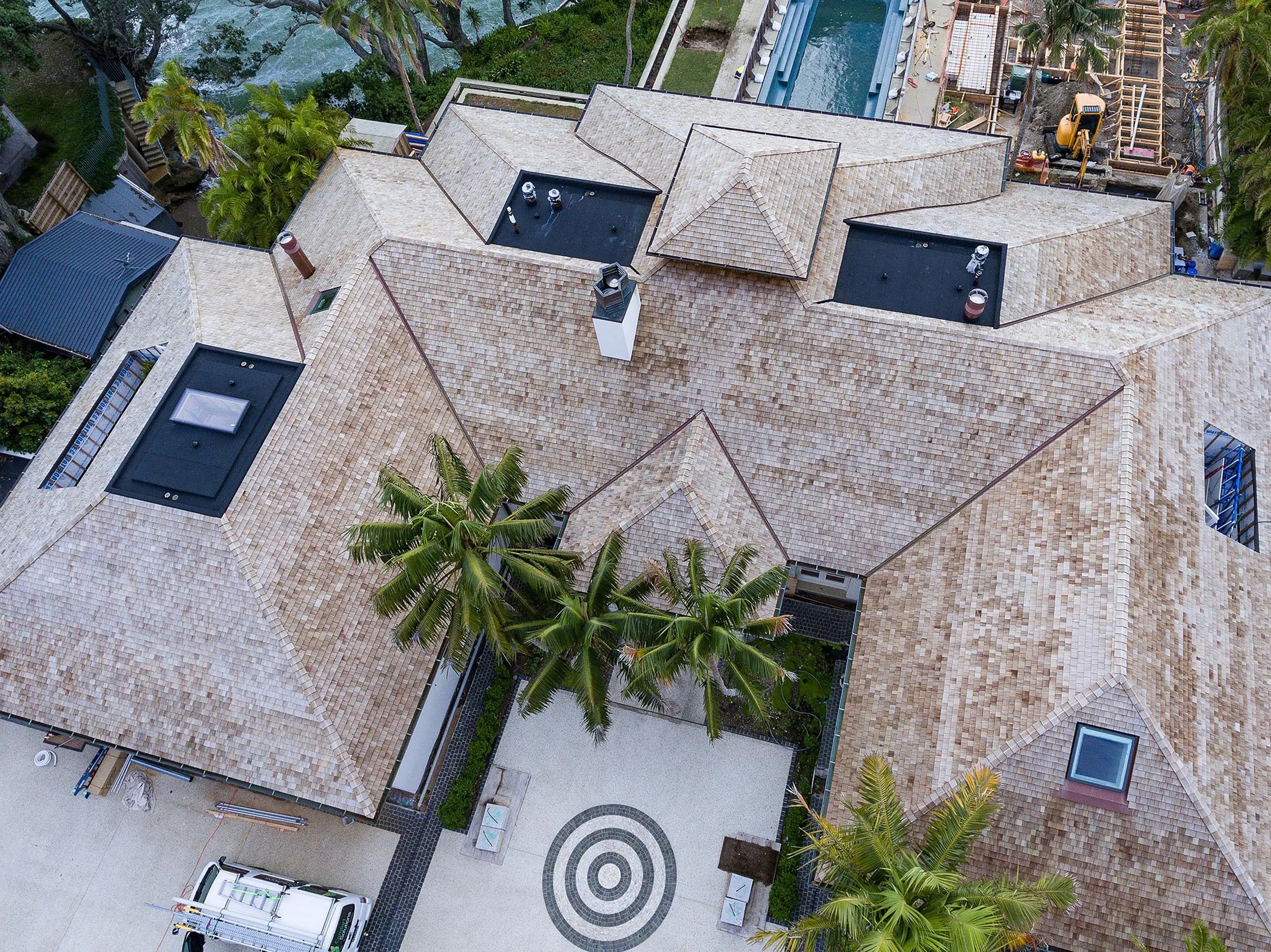 Aerial view of a large house with multiple rooftops, a patterned driveway, trees, and a construction site nearby.