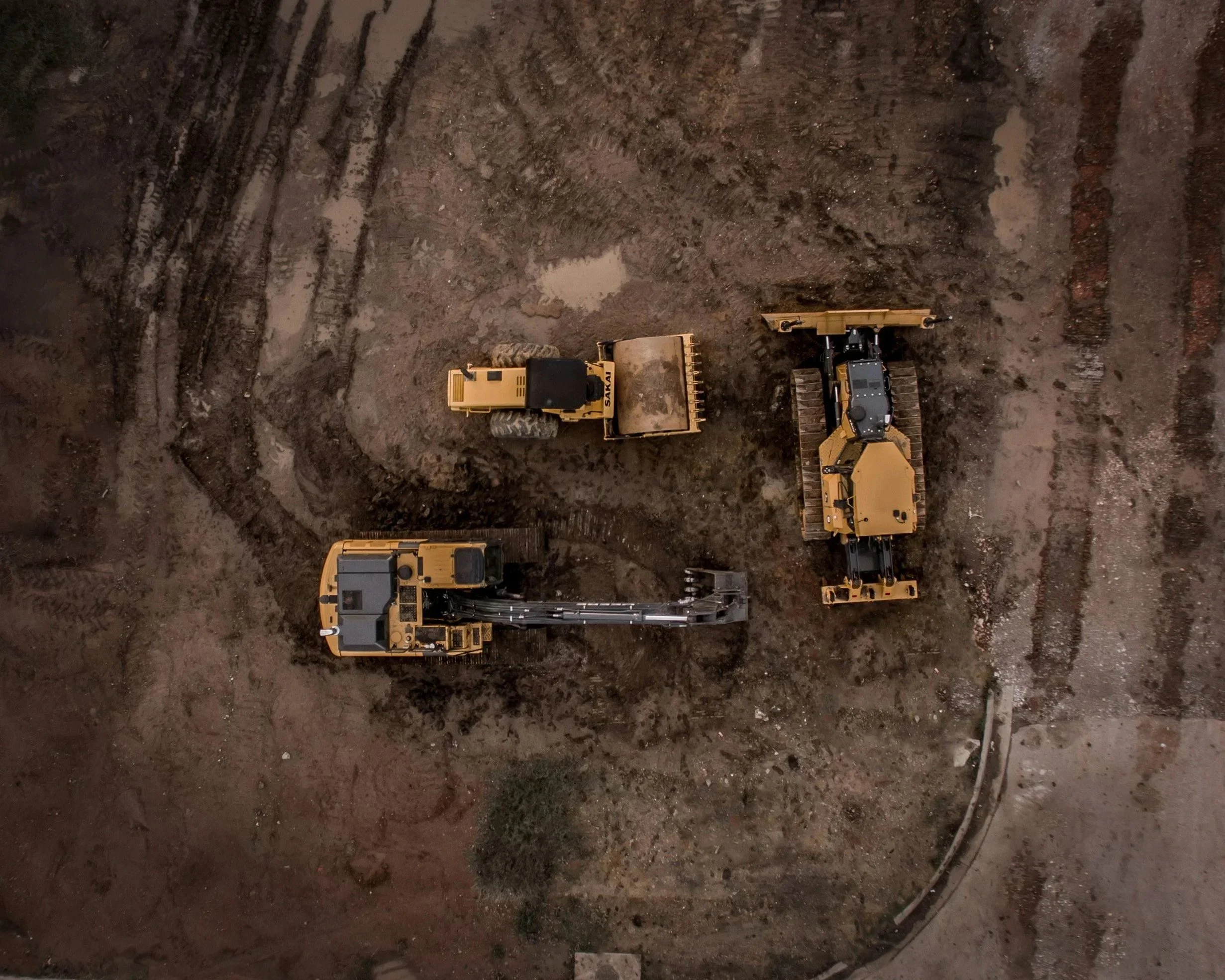 construction site with large yellow bulldozers moving dirt and soil, tire tracks in the excavated area.