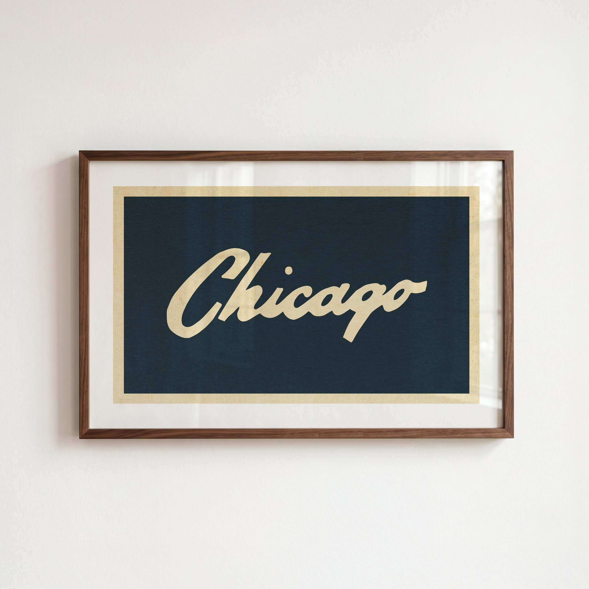Close-up of a framed poster with a beige background and part of the word 'Chucas' visible, hanging on a plain white wall.