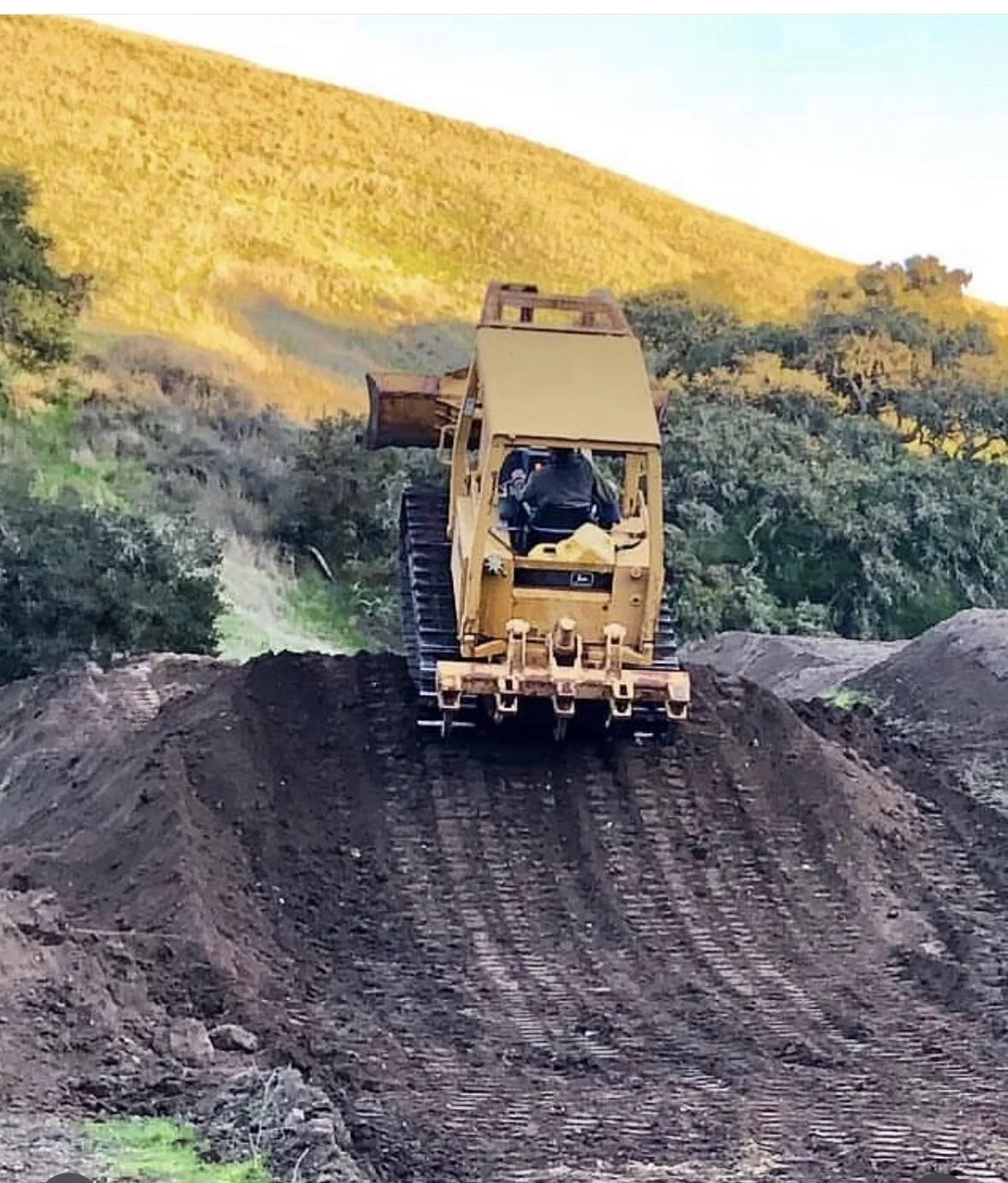man driving a tractor over the tip of a big dirt jump on a hillside