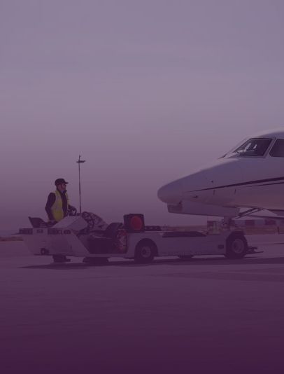 A man standing near a baggage cart loaded with luggage next to a small private jet on an airport runway.
