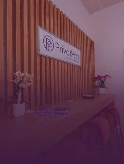 Interior of an office with a wooden slat wall, a sign reading 'PrivatPort,' a long wooden countertop with two flower vases, and red stools.