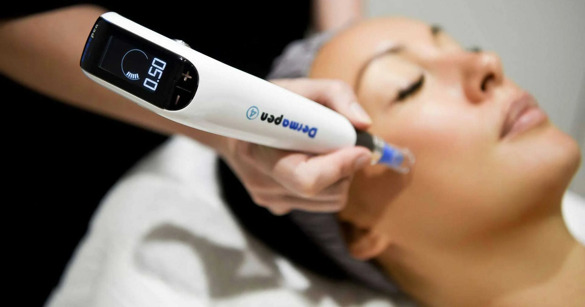 A woman receiving a procedure on her face with a DermoPen device held by a practitioner. The woman has her eyes closed and appears relaxed.