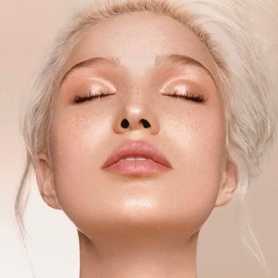 Close-up of a woman's face with light makeup, eyes closed, and platinum blonde hair swept back.