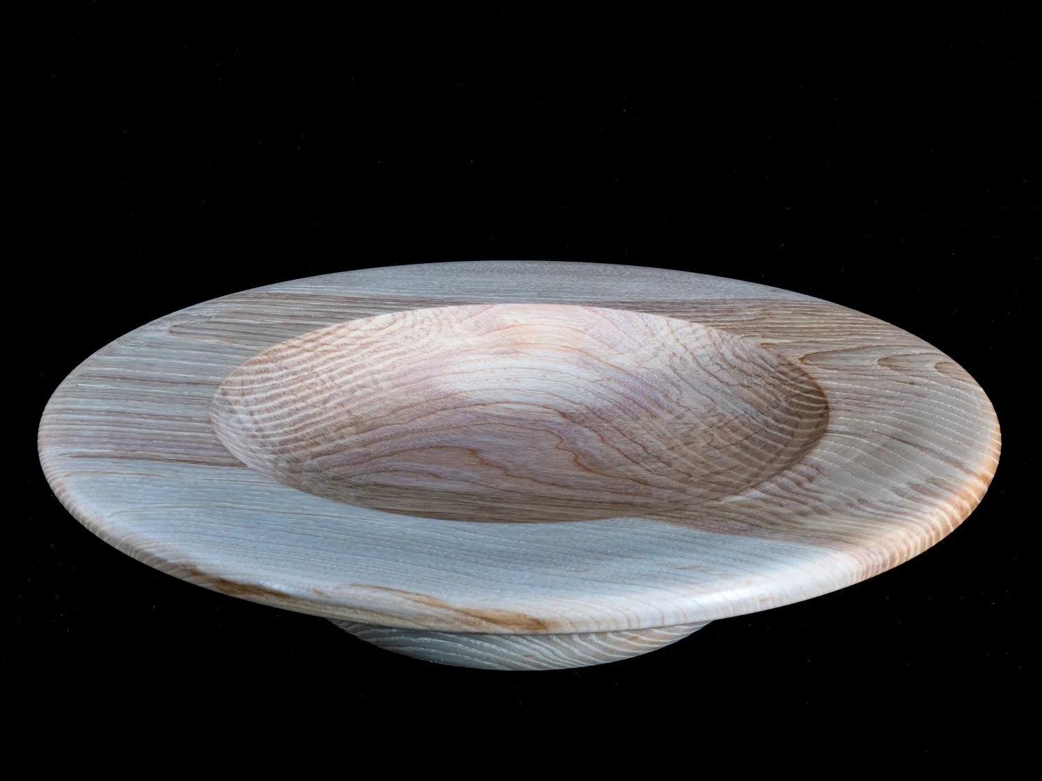 A wooden bowl with a shallow, circular shape and a smooth, polished surface, placed against a black background.