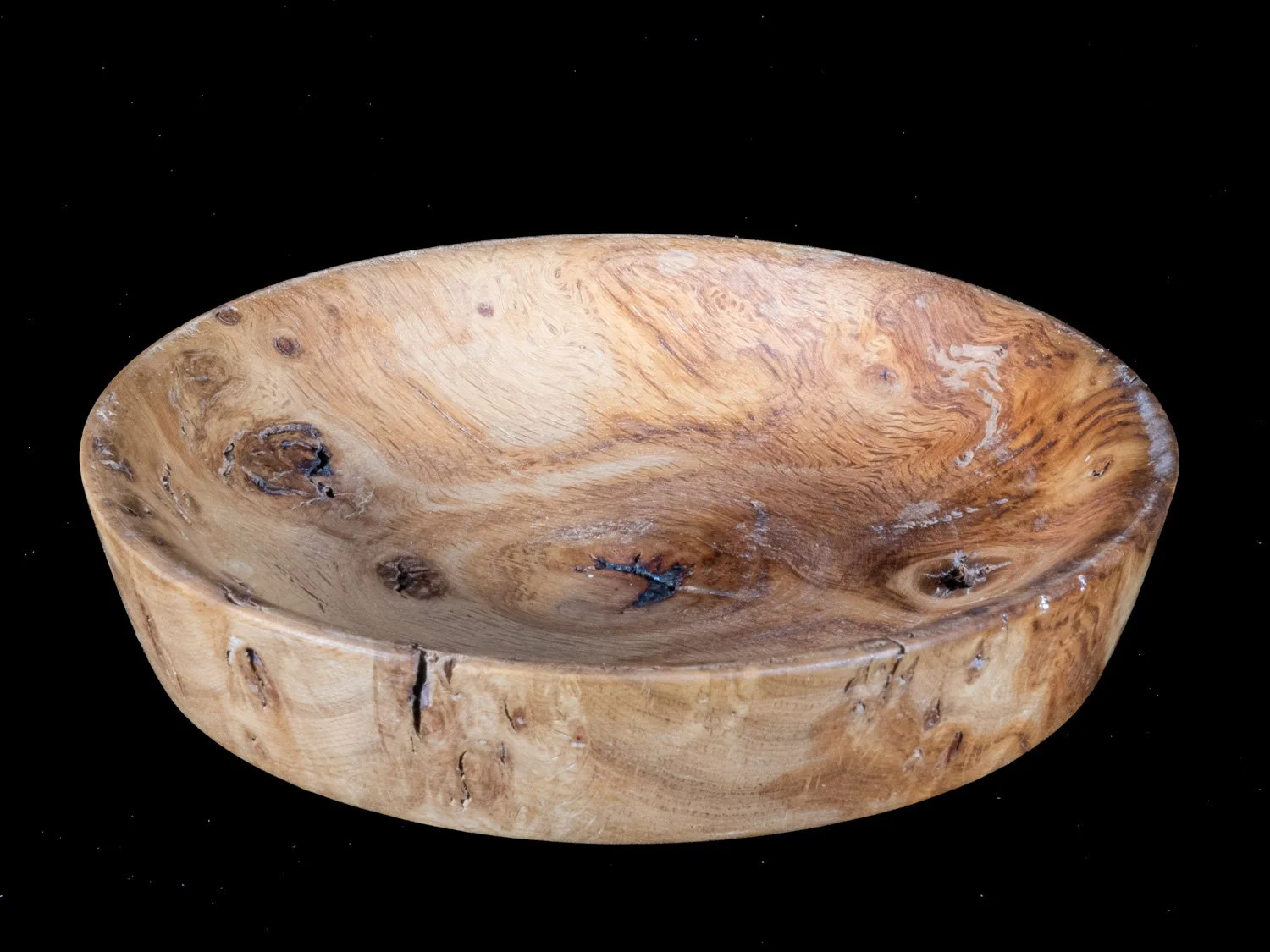 A round wooden bowl with natural wood grain and knots, placed against a black background.