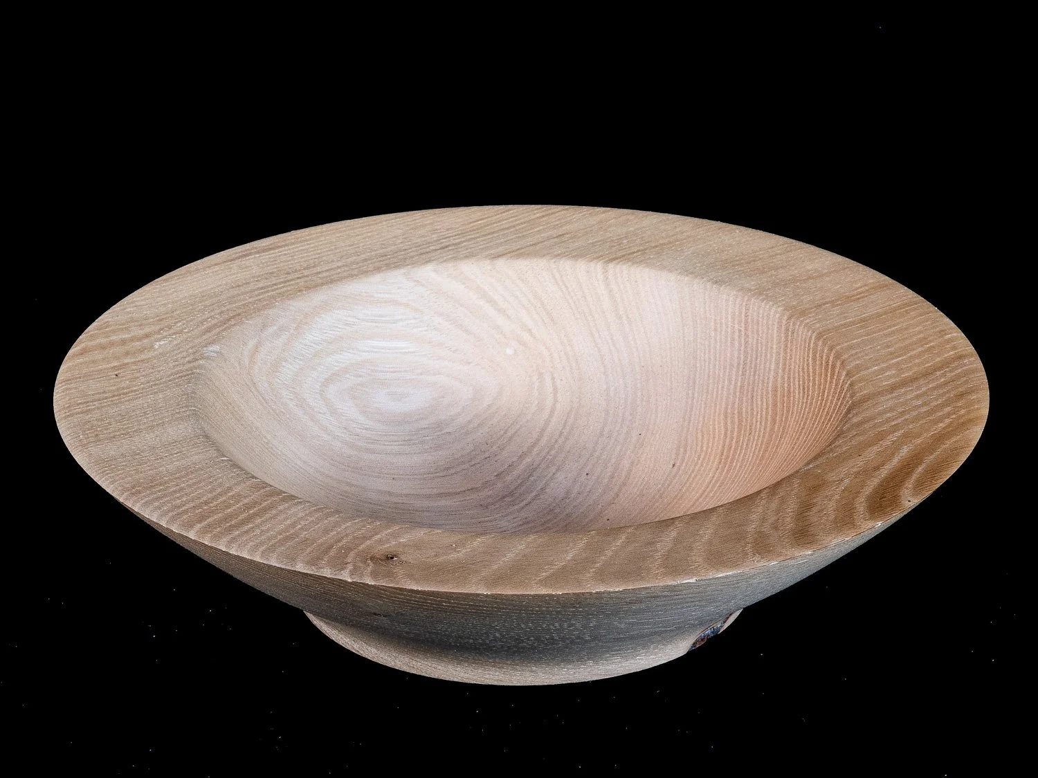 Close-up of a wooden bowl with a smooth, rounded interior and visible wood grain, set against a black background.