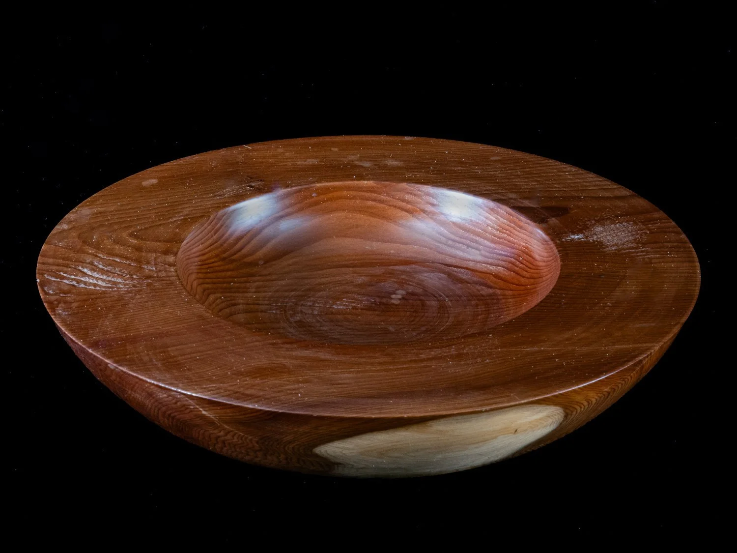 A wooden bowl with a smooth, polished surface, showing visible wood grain patterns, against a black background.