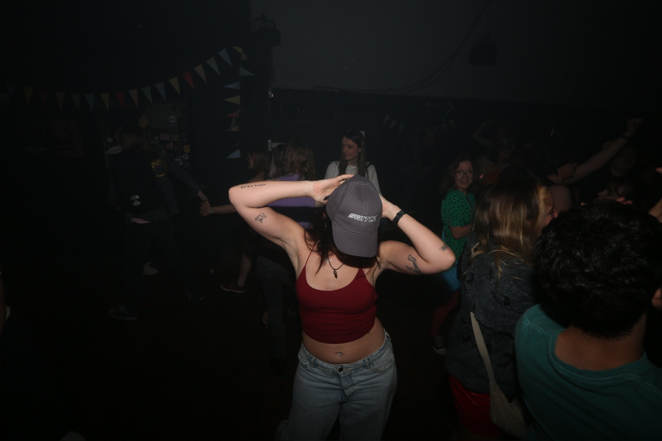 People dancing and socializing in a dimly lit party or nightclub with bunting decorations hanging from the ceiling.