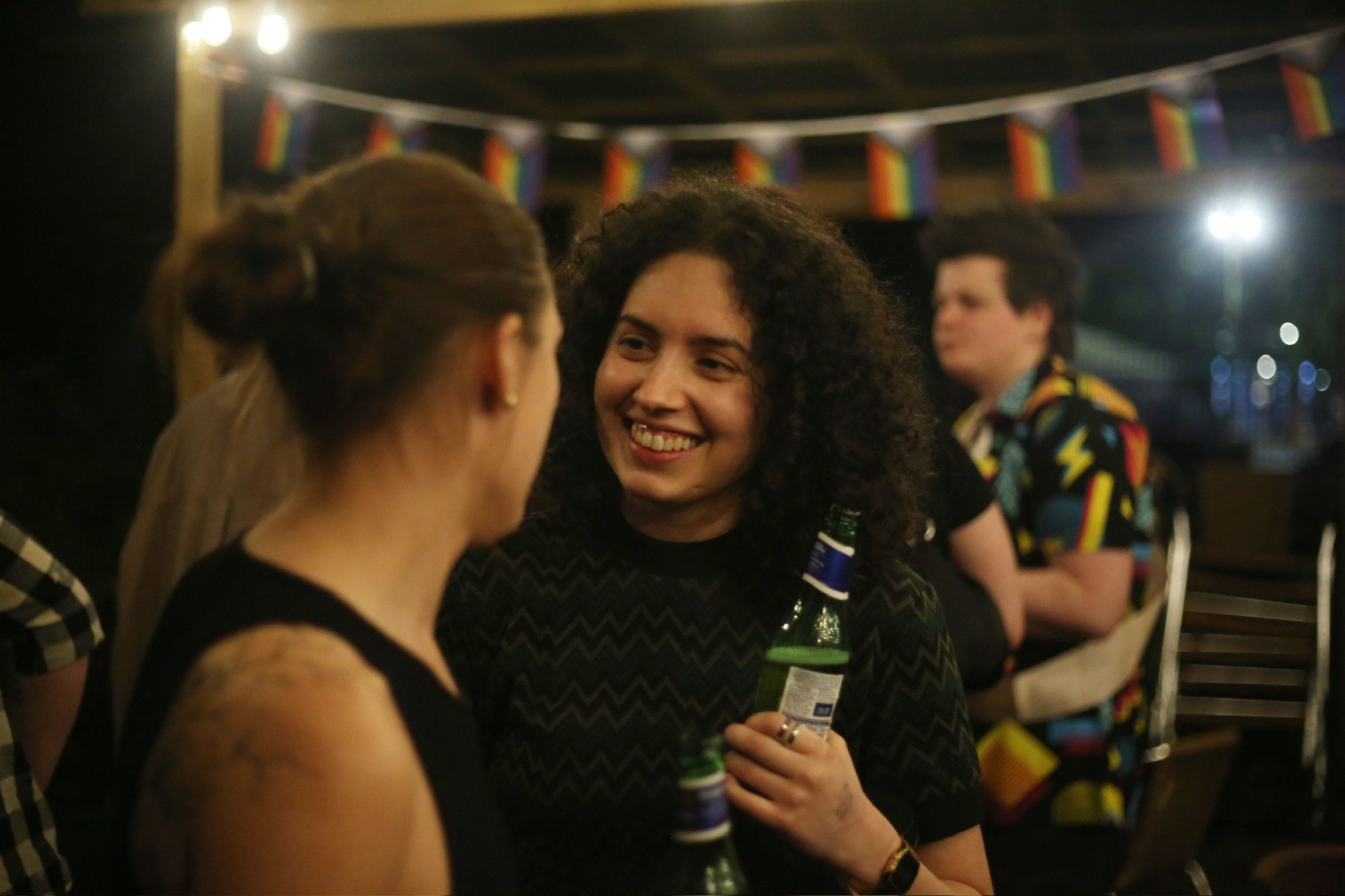 Group of people socializing at a celebration, with rainbow flags hanging in the background.