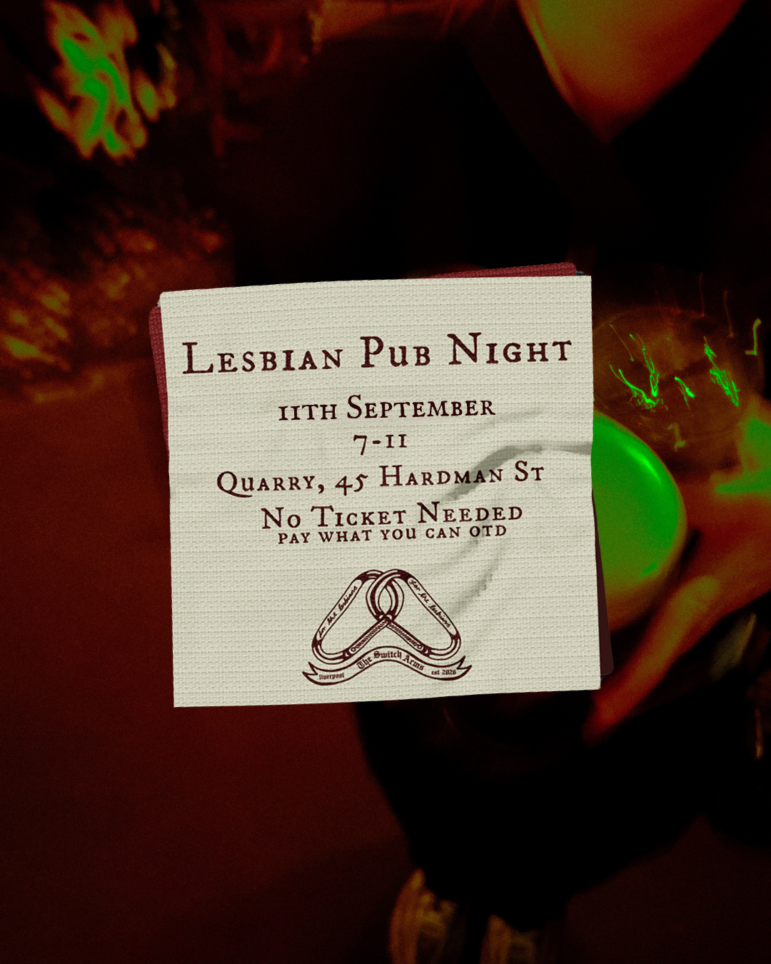 Person holding a flyer for a lesbian pub night event at a bar, with two people sitting close together in the background.