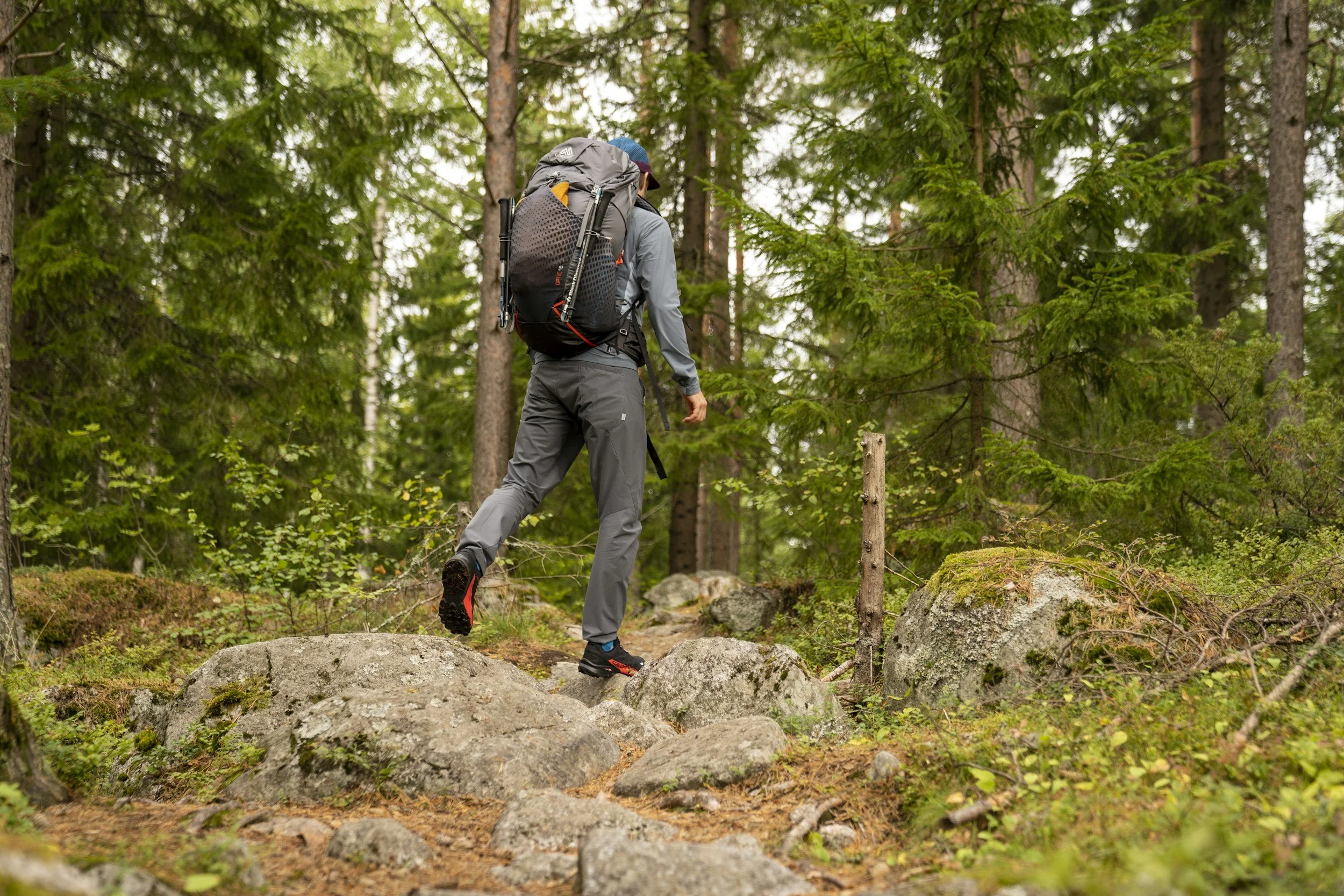 En person som vandrar på en stengång i skogen, bär på en stor ryggsäck och använder vandringsstavar.
