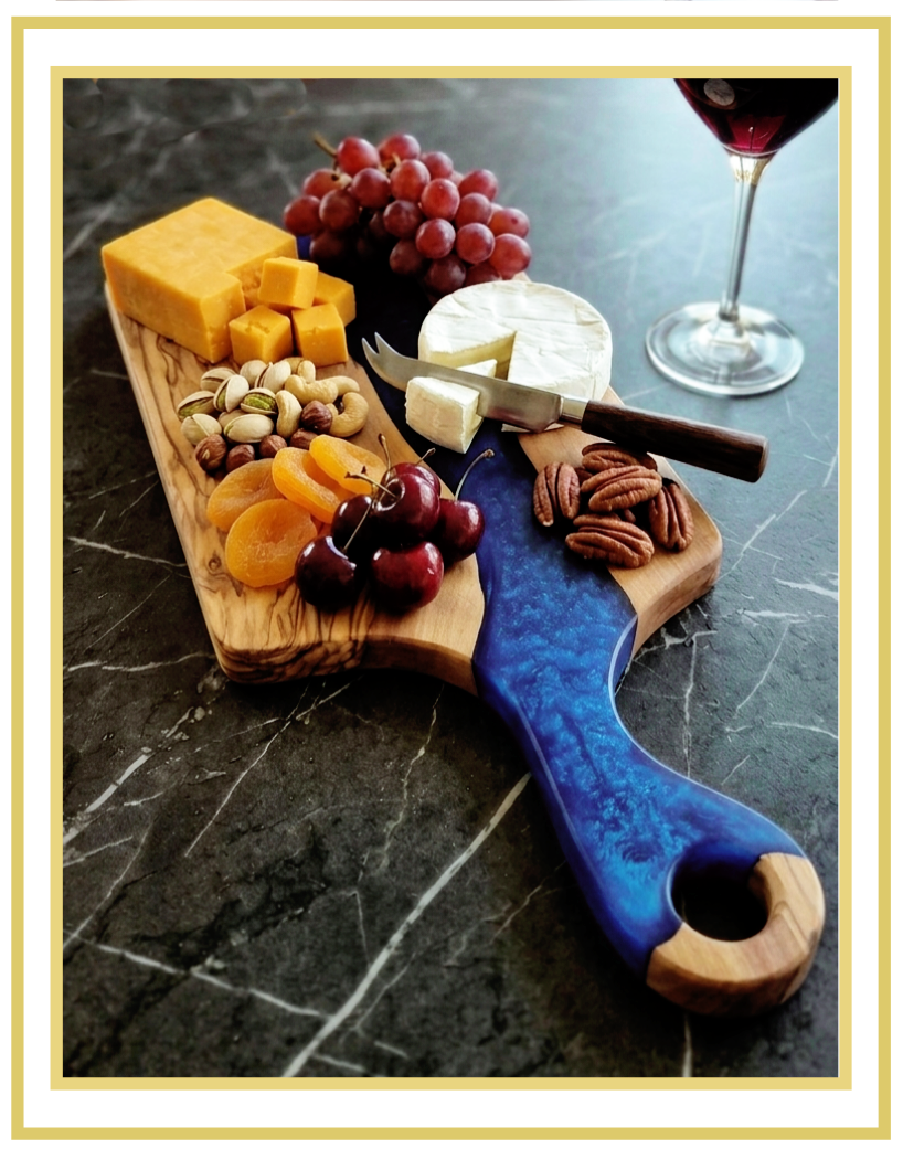 Handcrafted live-edge serving and grazing board arranged with cheese, fruit, nuts and dried apricots beside a glass of red wine.