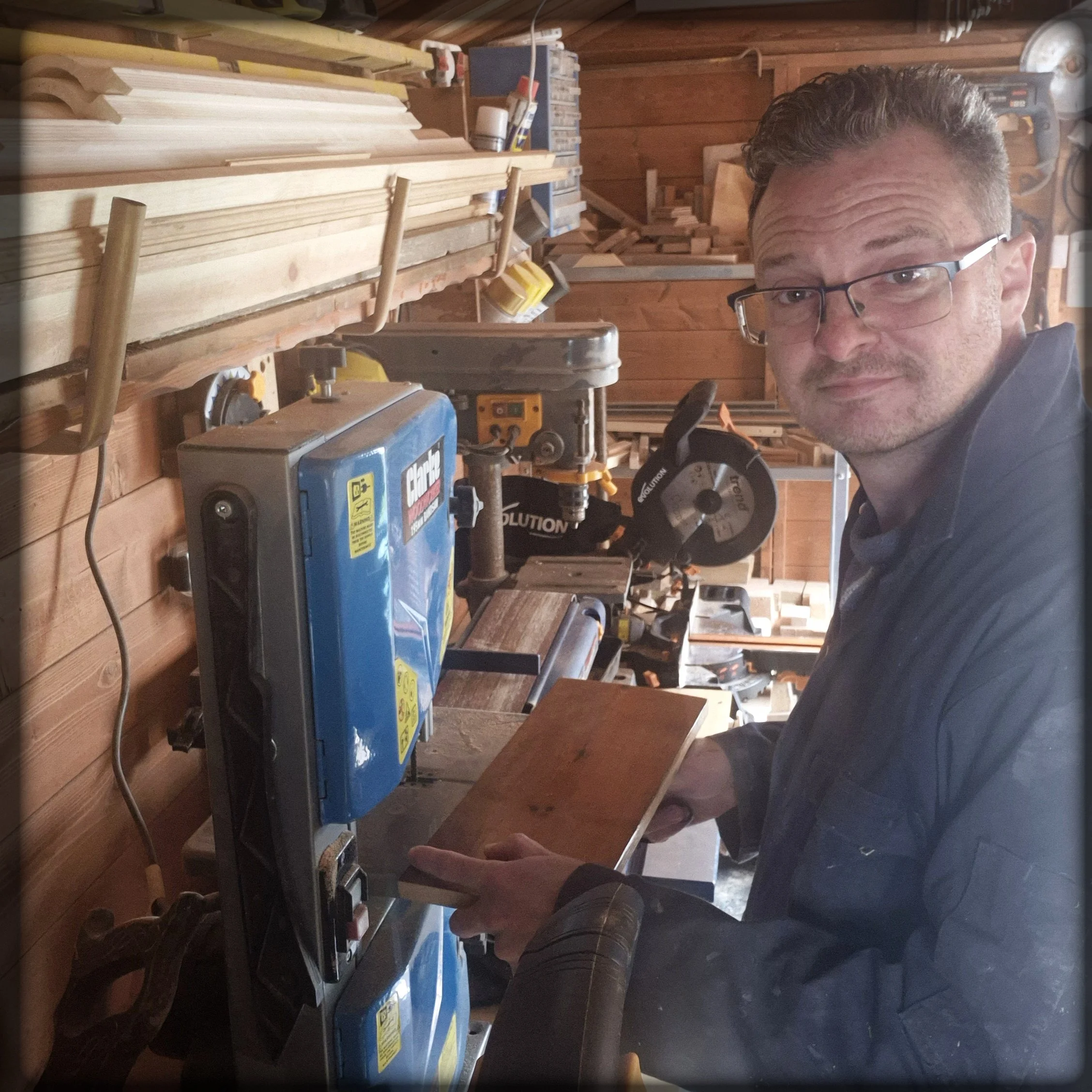 Woodworking workshop with various tools and a man in glasses looking at the camera