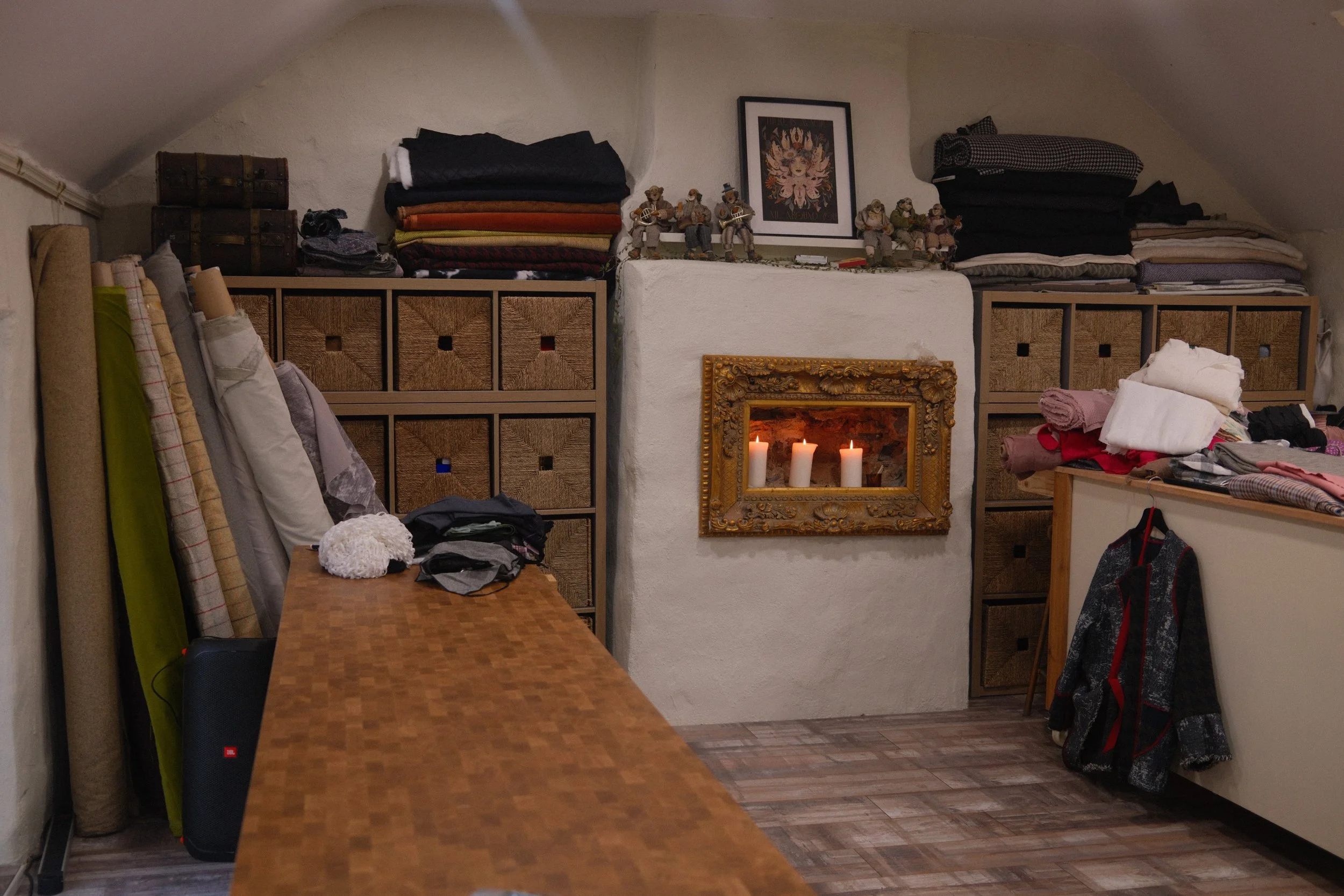 Room with a fire in the fireplace, shelves with folded clothes, framed artwork on the wall, and various items including blankets, hats, and a speaker. Mise Tusa Clarinbridge design galway ireland meritta
