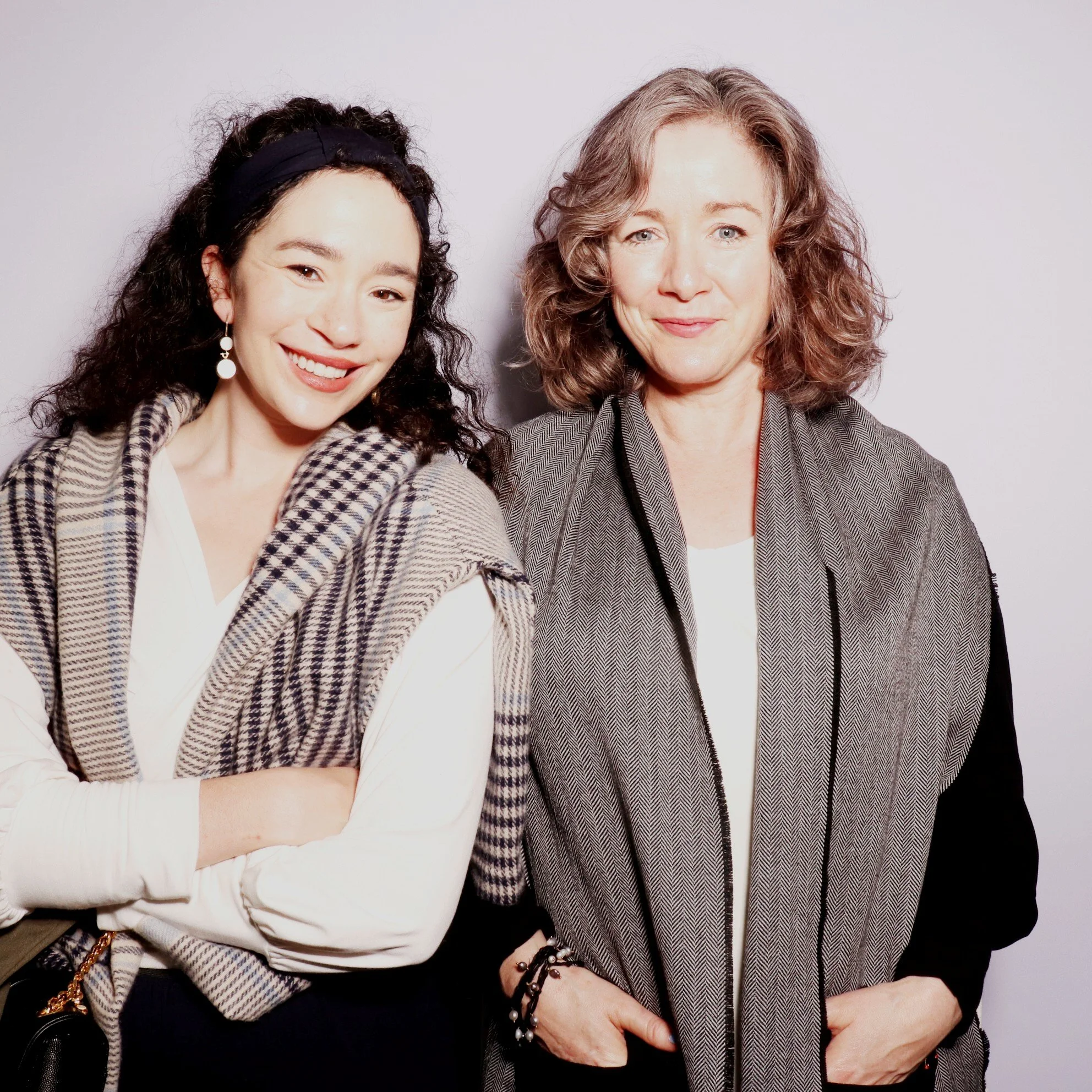 Two women smiling, one with dark curly hair and wearing a black headband, patterned jacket, and white blouse; the other with light curly hair, wearing a Mise Tusa Clarinbridge design galway ireland meritta