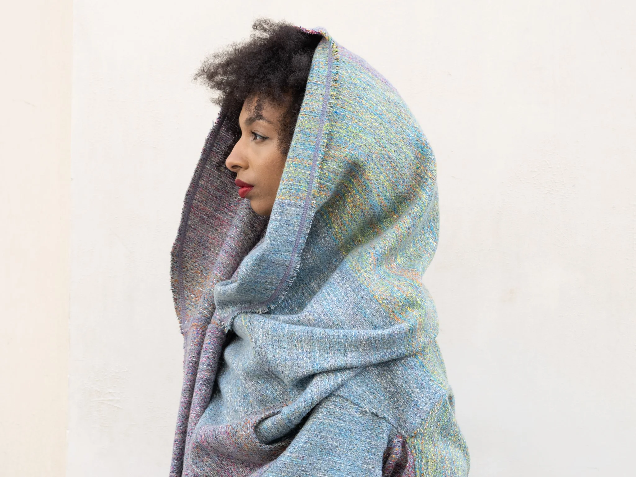 Side view of a woman with natural curly hair, wrapped in a colorful gradient scarf, standing against a plain light background. Mise Tusa Clarinbridge design galway ireland meritta