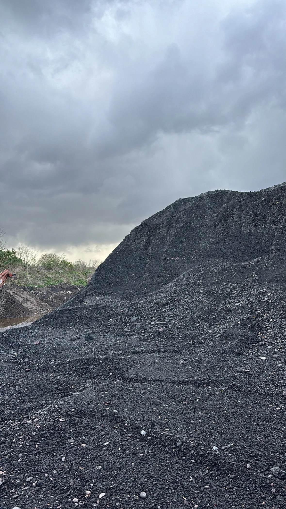 A large mound of black gravel or coal outside on a cloudy day with dark, overcast skies