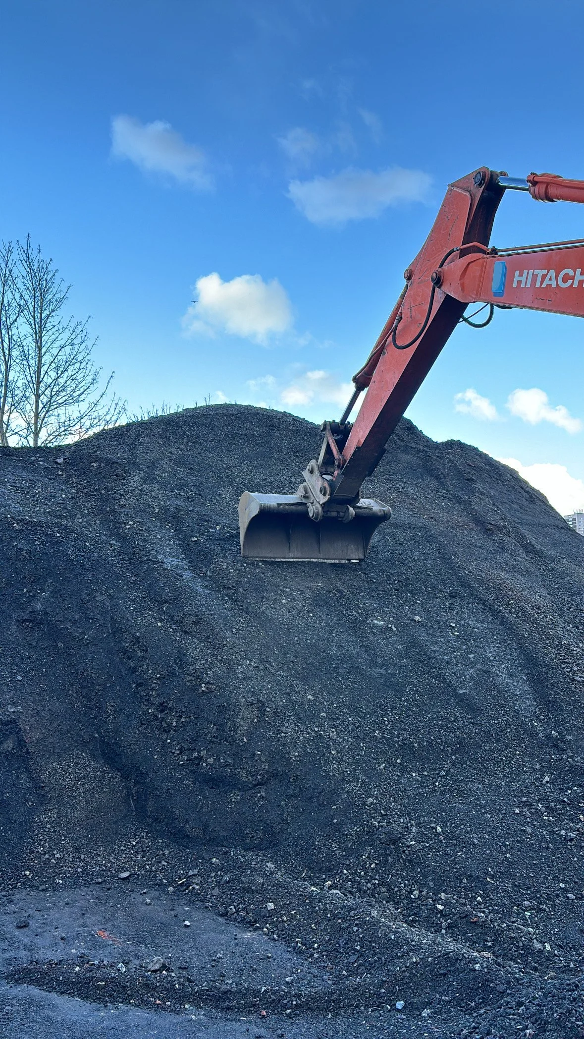 An orange excavator bucket resting on a large pile of dark gravel or dirt.