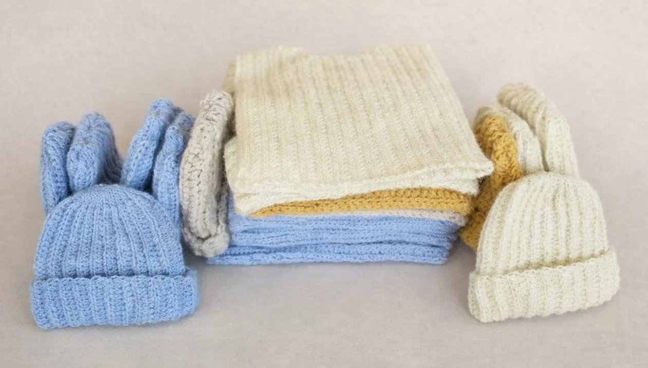 A pile of crocheted vests and hats in cream, mustard and tan colours