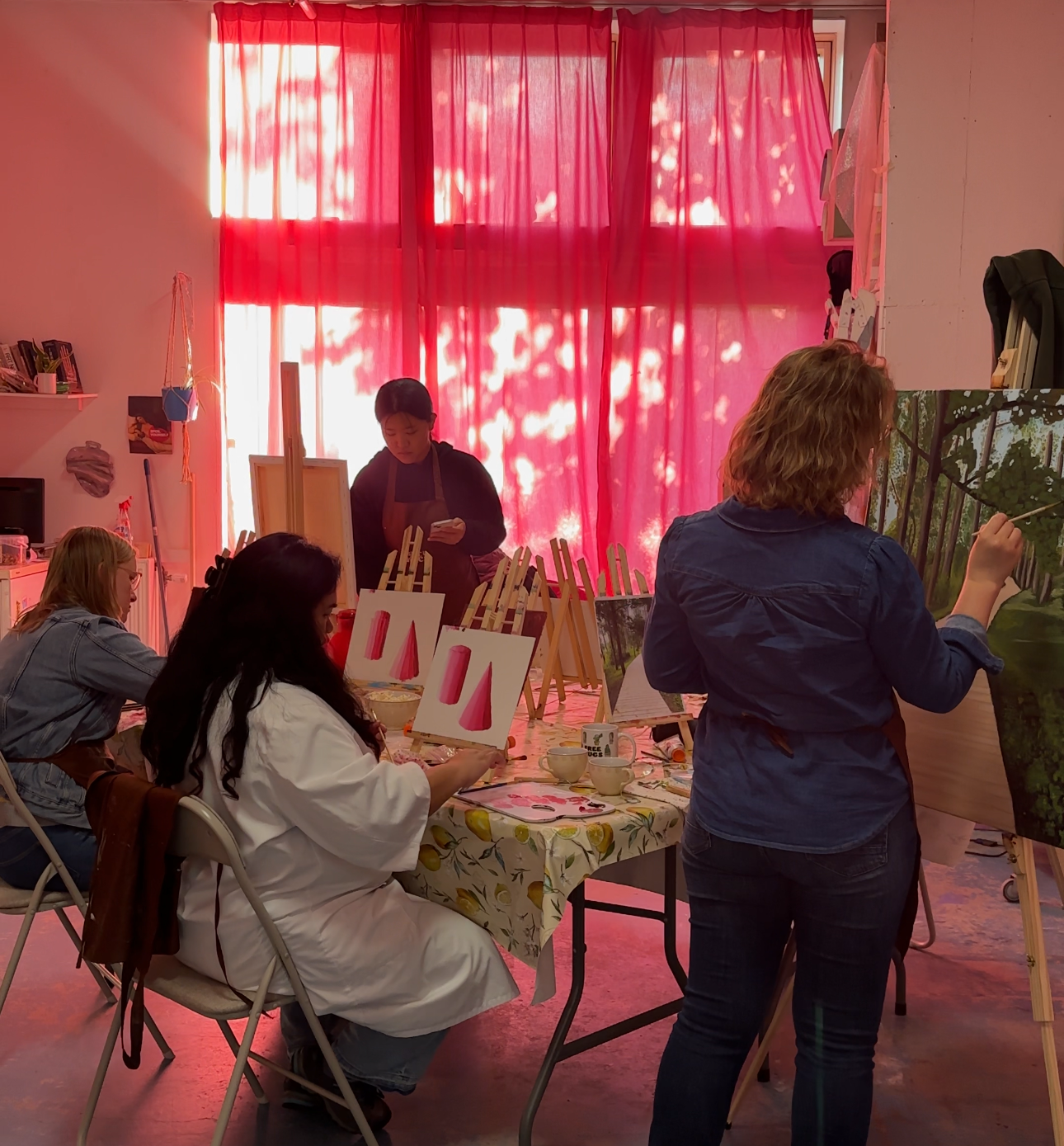 People painting tree and landscape scenes in an art class with pink curtains in the background.