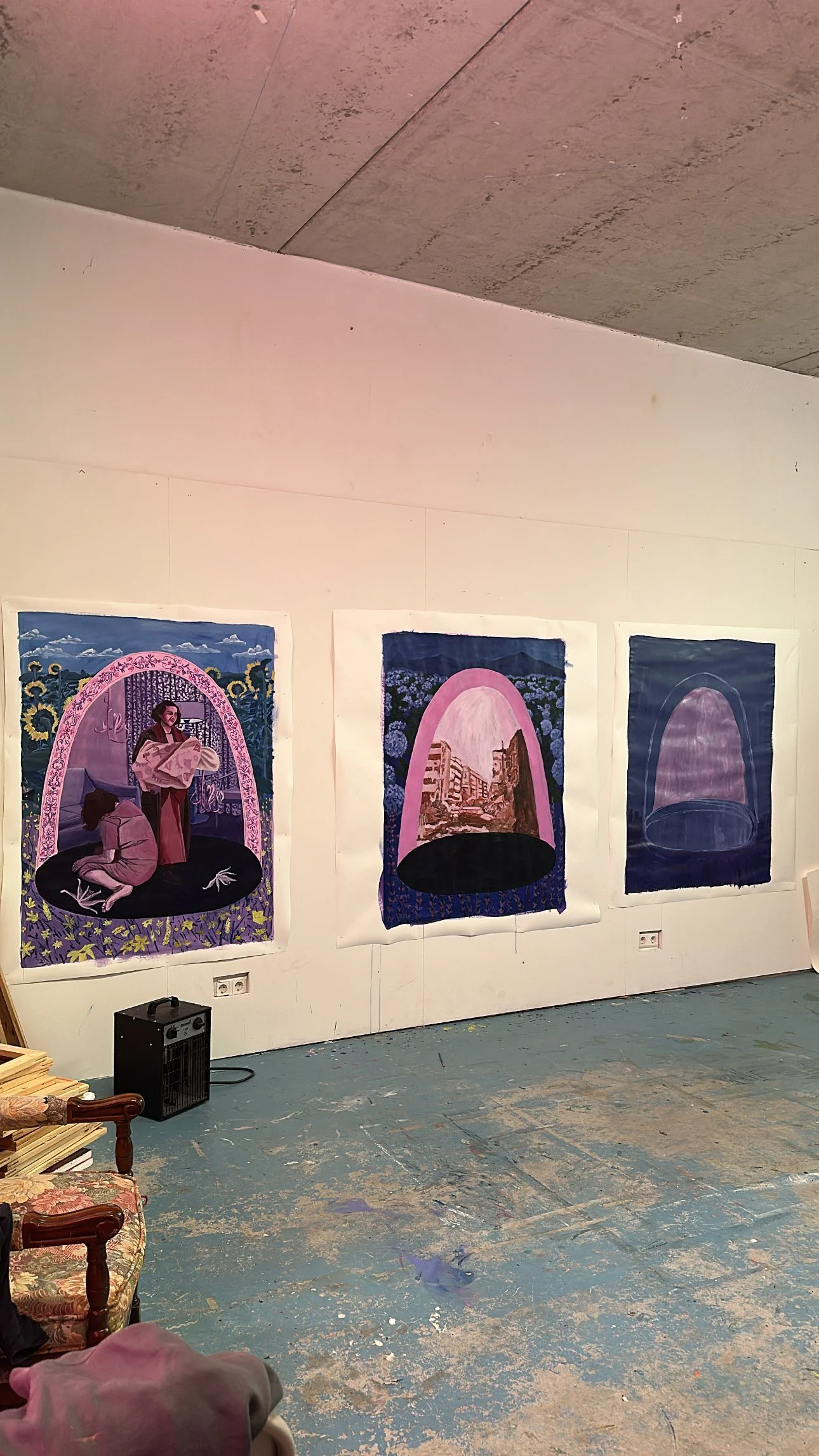 Three large, detailed paintings displayed on a white wall in an art gallery. The paintings depict surreal scenes with arches and various imagery. The gallery has a concrete floor with paint splatters and some furniture visible.