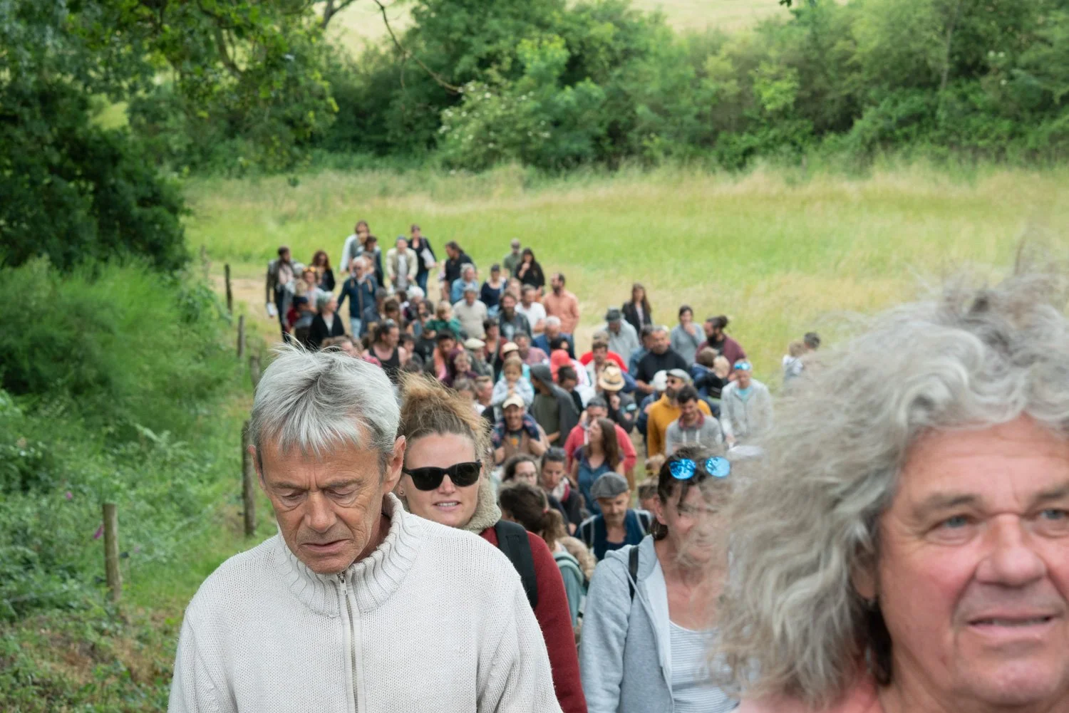 Gros groupe de personnes marchant dans la nature verdoyante, avec des arbres et de l'herbe, probablement lors d'une sortie ou d'une promenade en forêt.